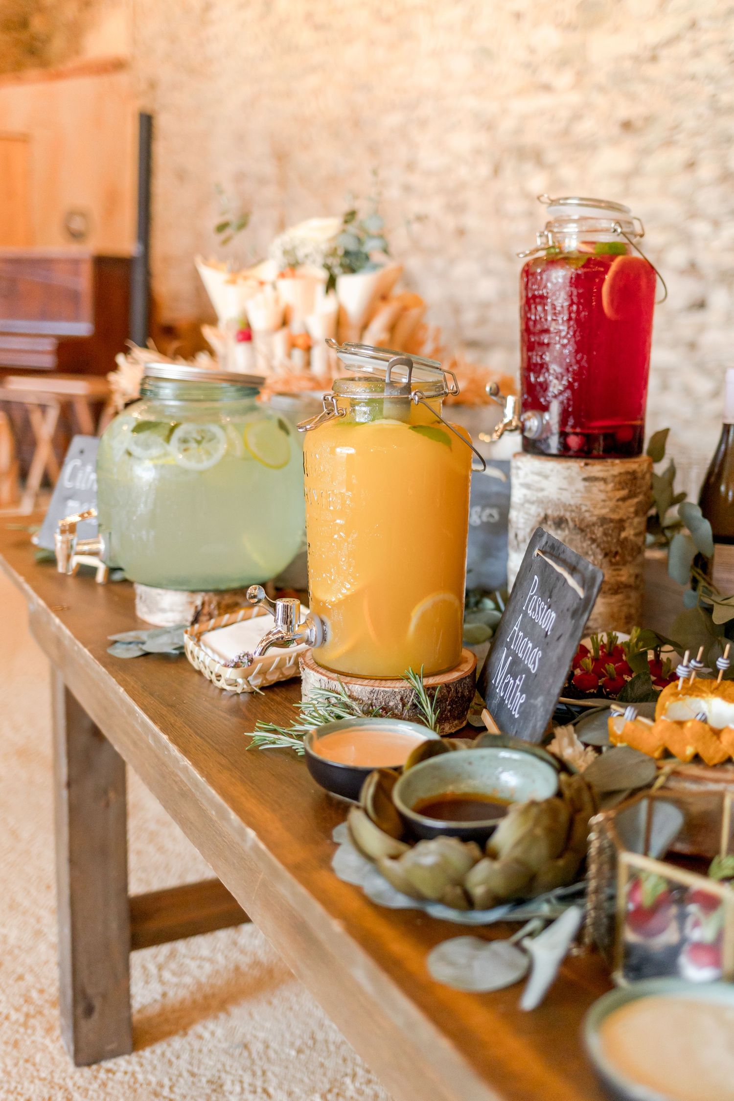 Drink station with colorful beverages in large glass dispensers against stone wall backdrop.