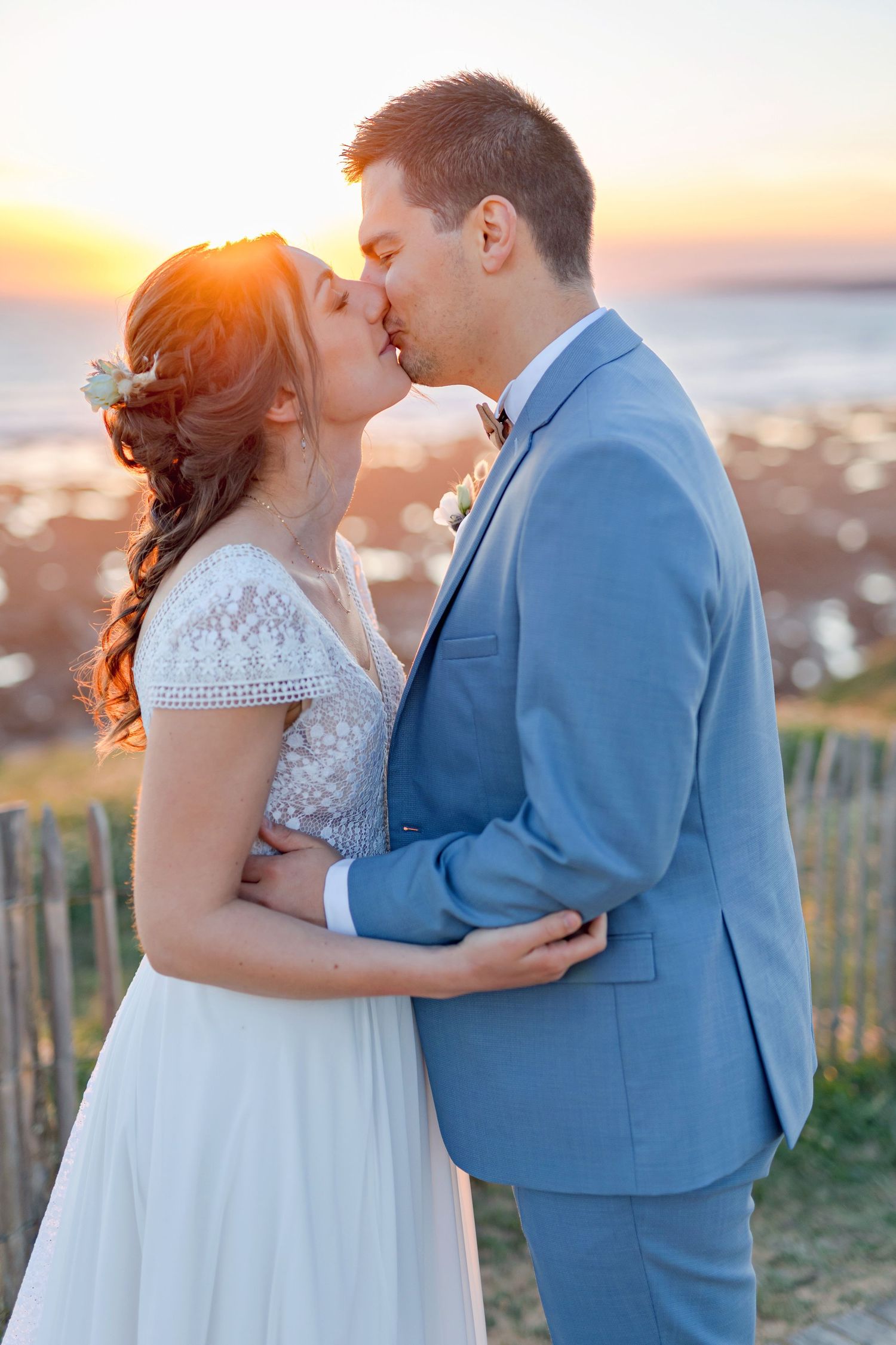 Romantic sunset kiss between newlyweds on coastal cliffside boardwalk.