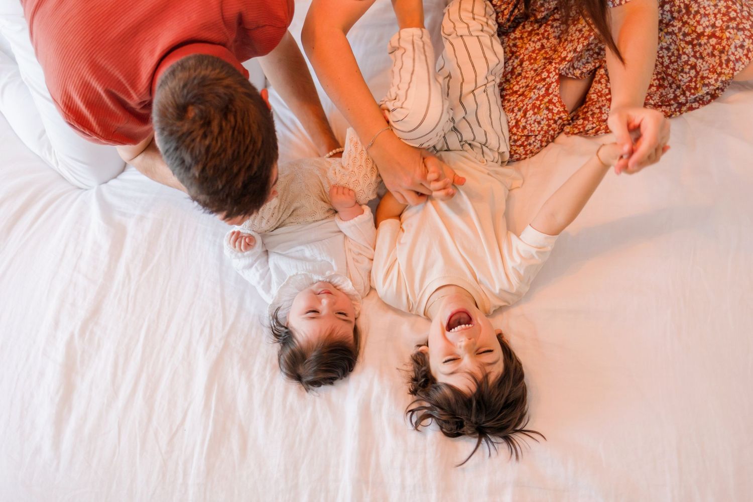 Family members playing and laughing together while lying on white bedding.