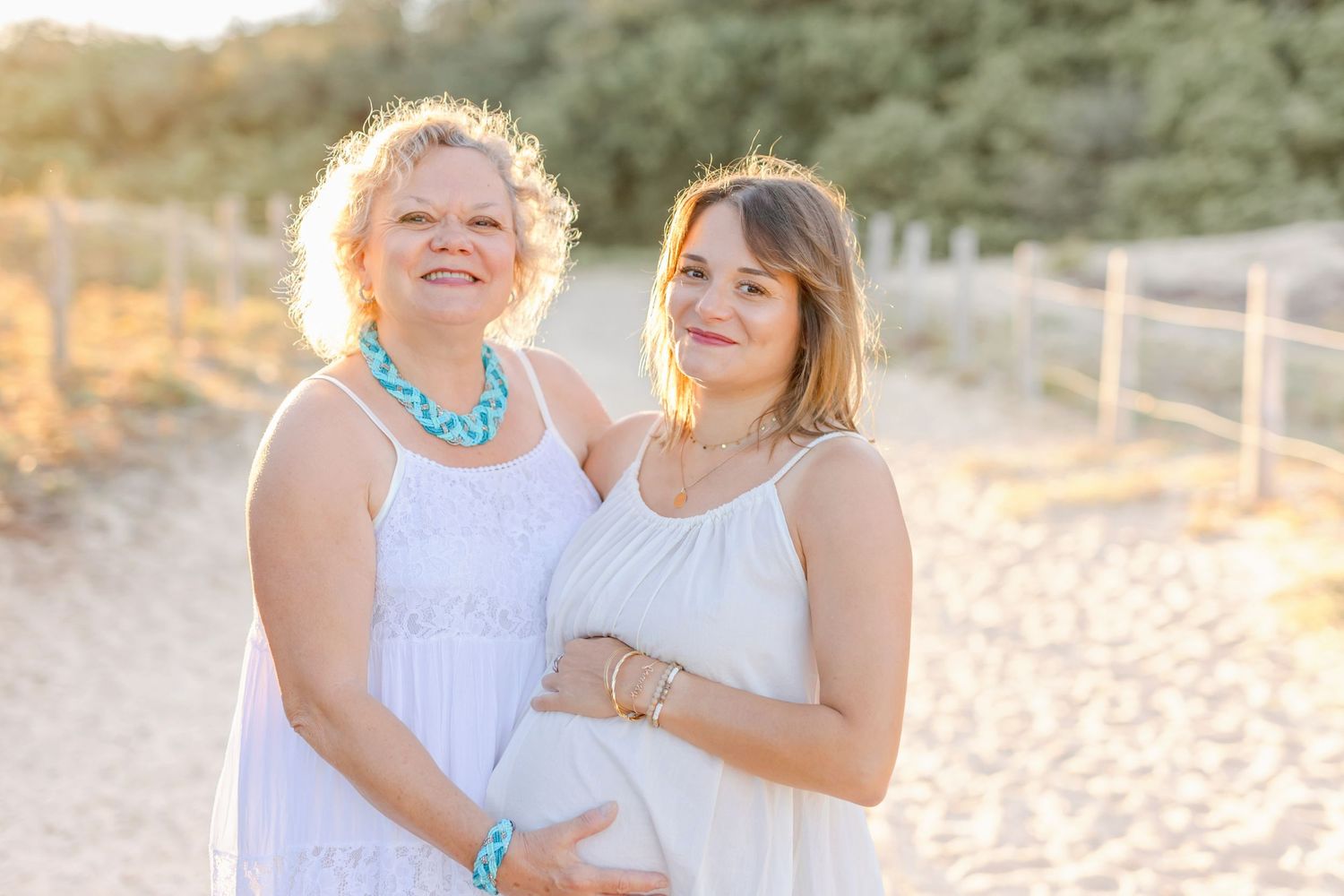 Two people in white dresses share a joyful moment on a beach path.