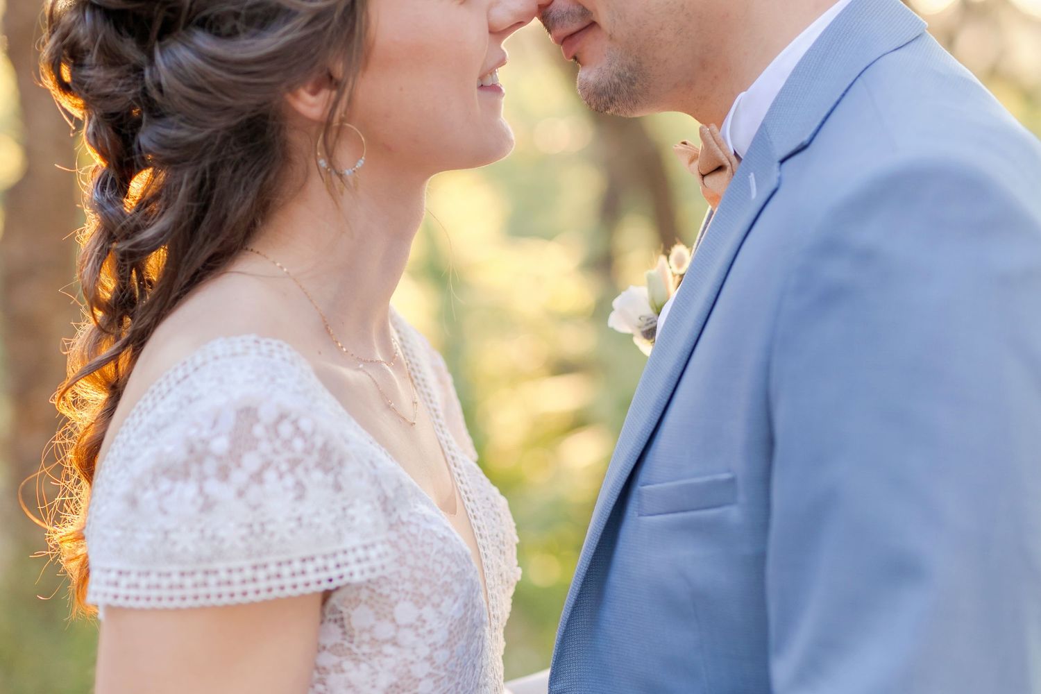 Close-up wedding portrait showing intricate lace details of a bridal gown and light blue suit.