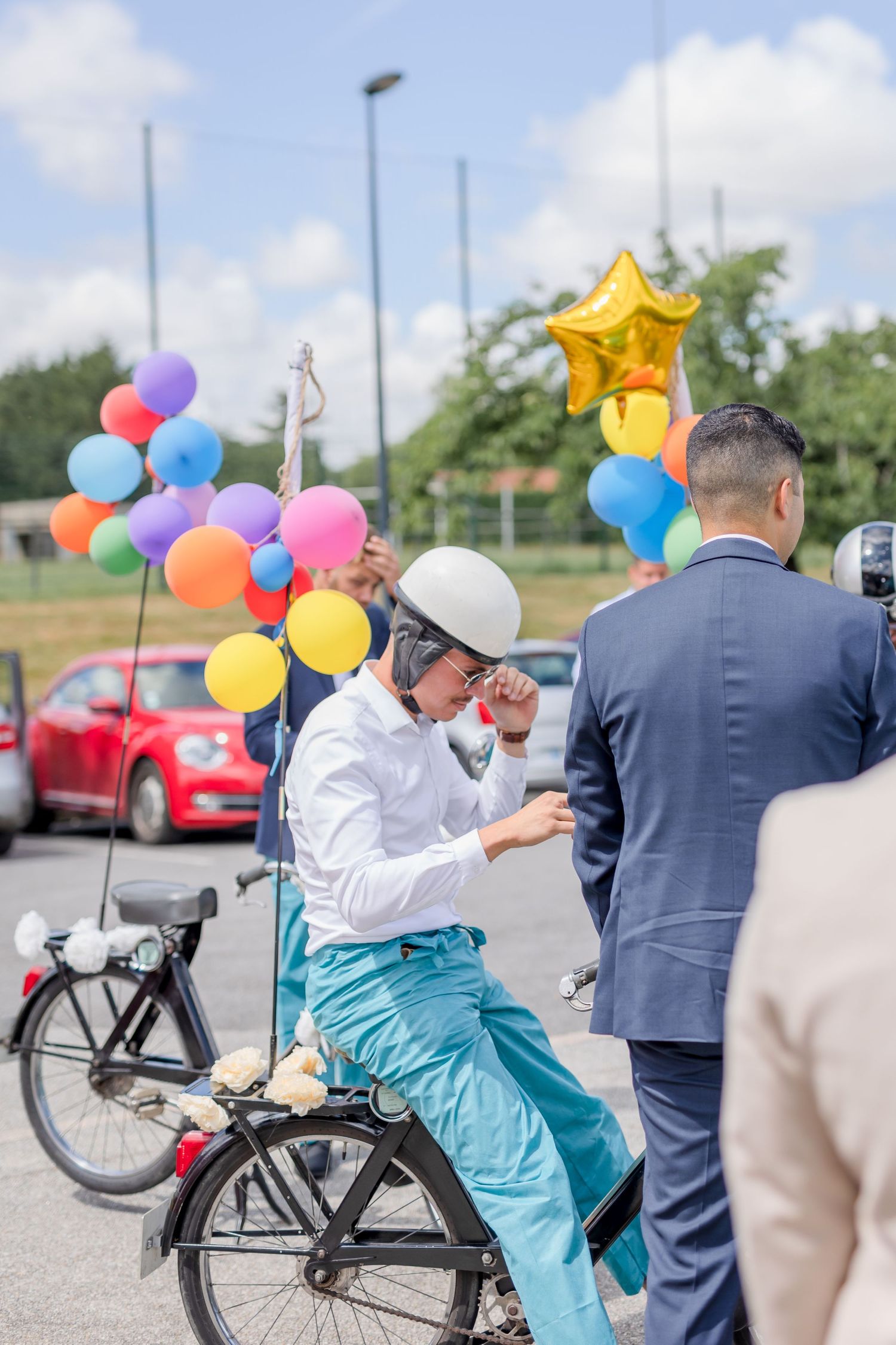Person sits on bicycle decorated with colorful balloons at outdoor event.