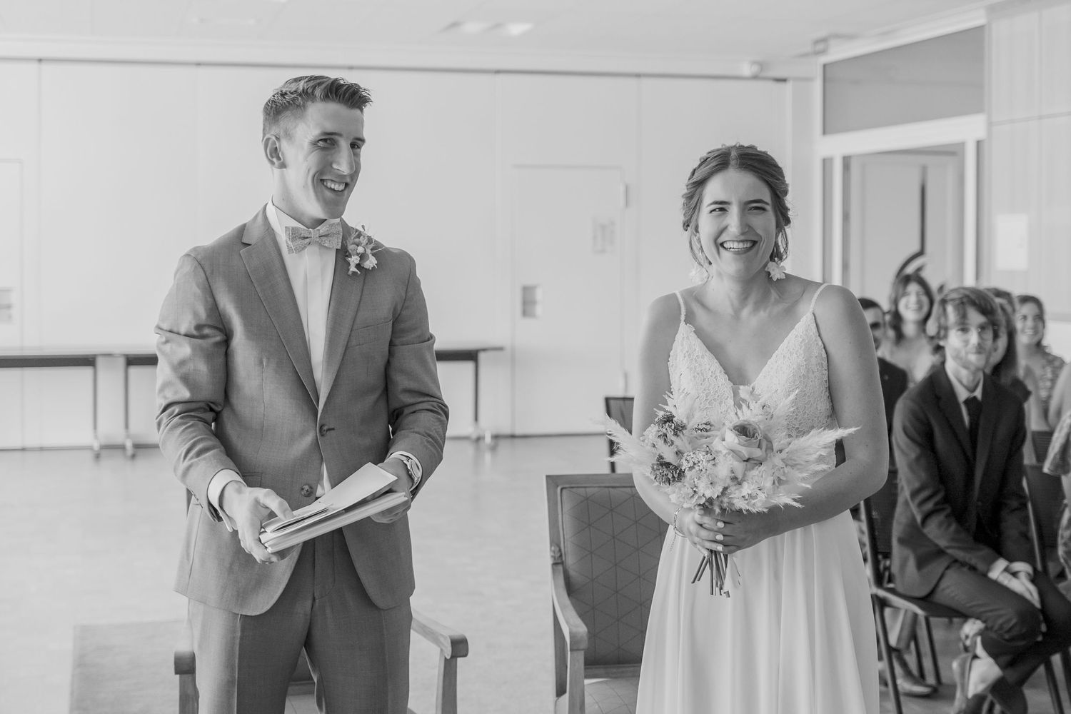 Wedding ceremony celebration with attendees gathered in bright indoor space.