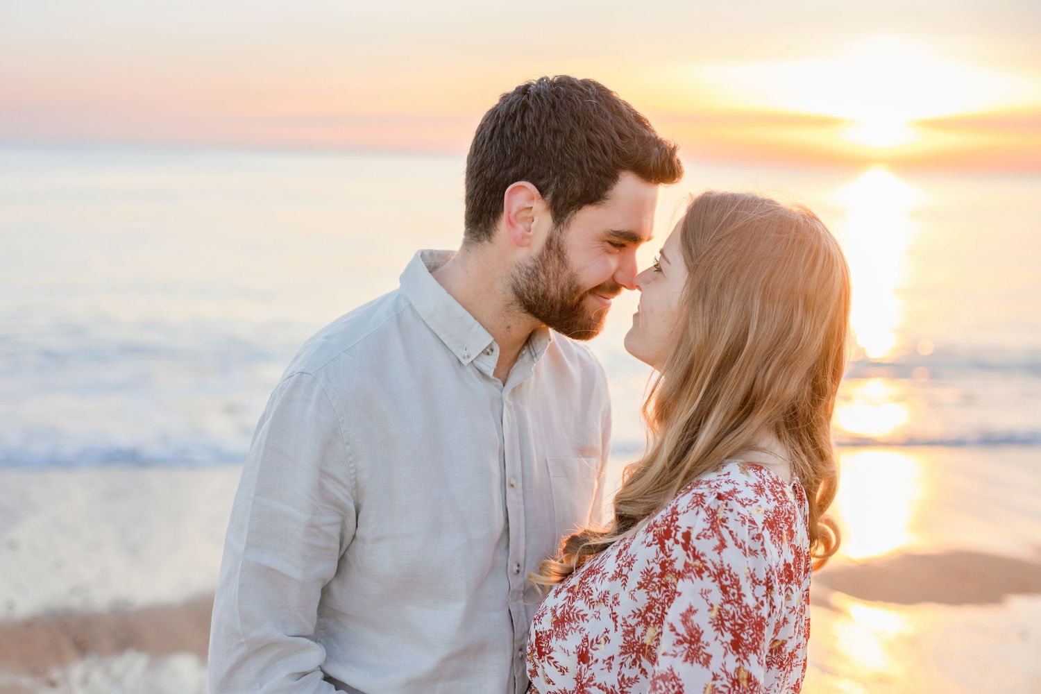 A romantic couple shares a close moment on the beach during a golden sunset.