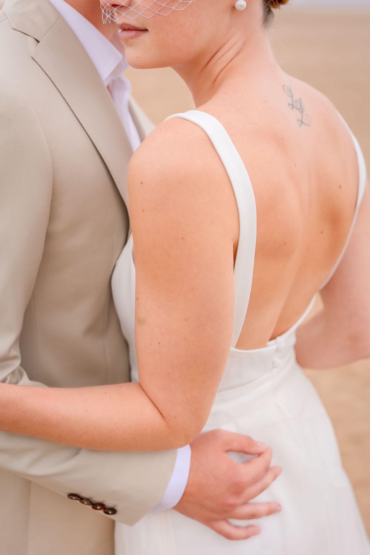 An intimate detail shot of a bride in a white dress showing her bare back and shoulder.