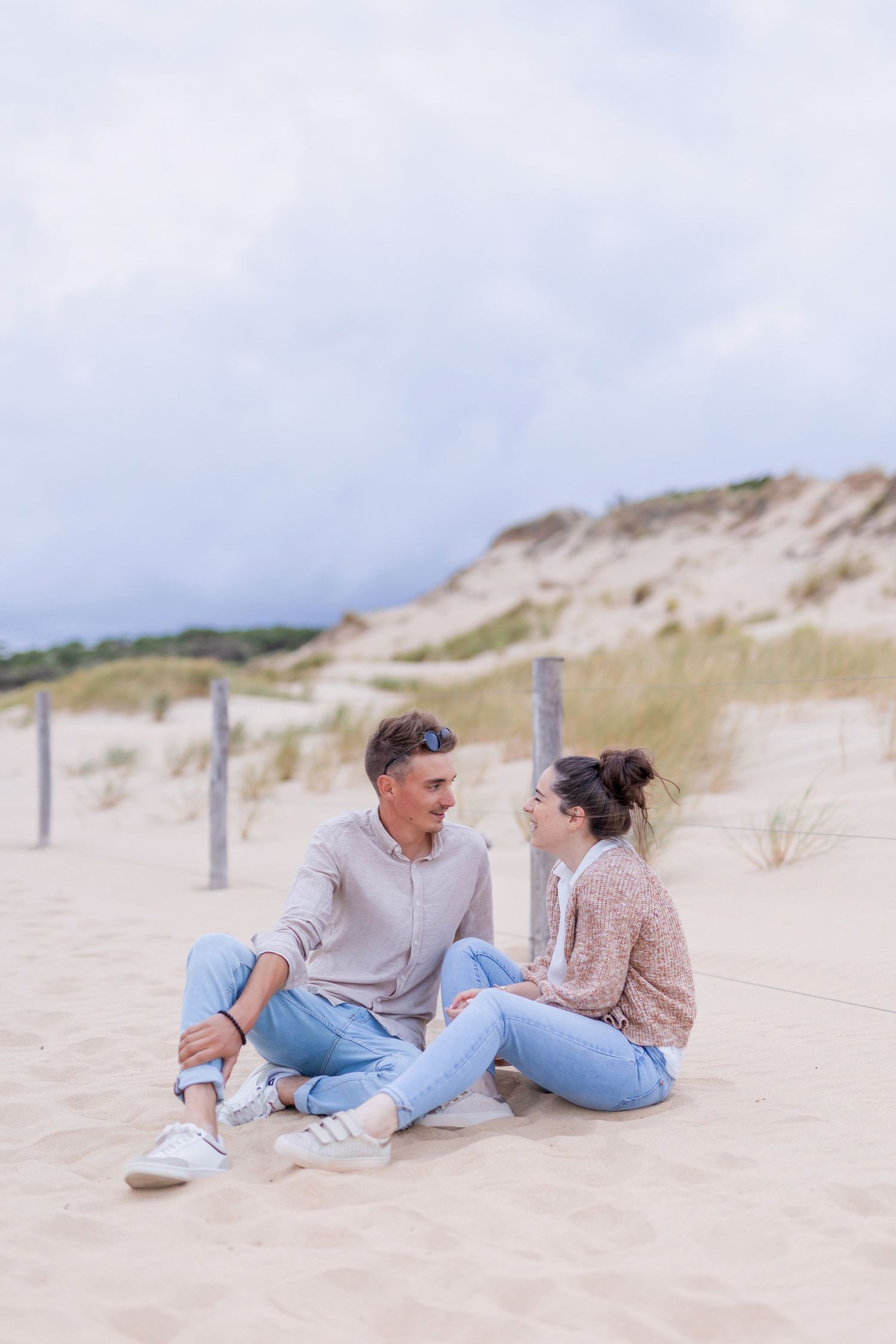 Relaxed couple lounging on sandy beach with coastal dunes in background.