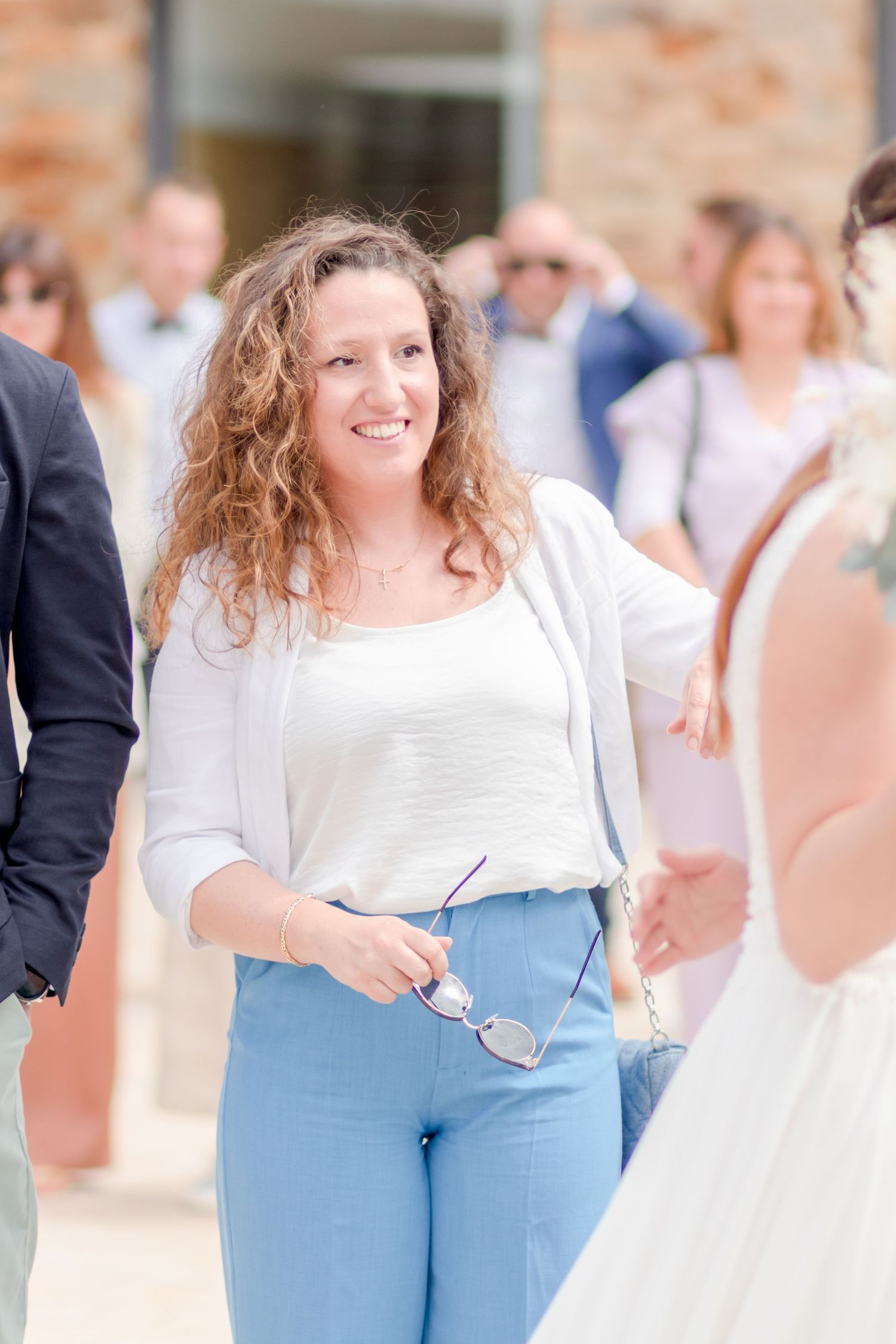 Woman in white top and light blue pants smiles at outdoor celebration.