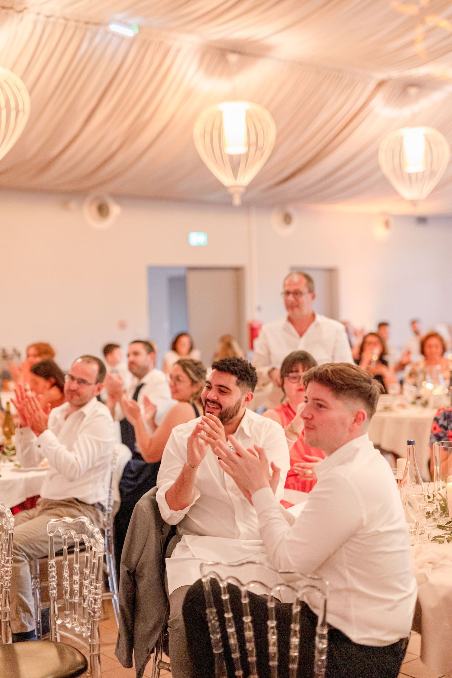 Wedding attendees clapping and smiling during celebration in a decorated white tent venue.