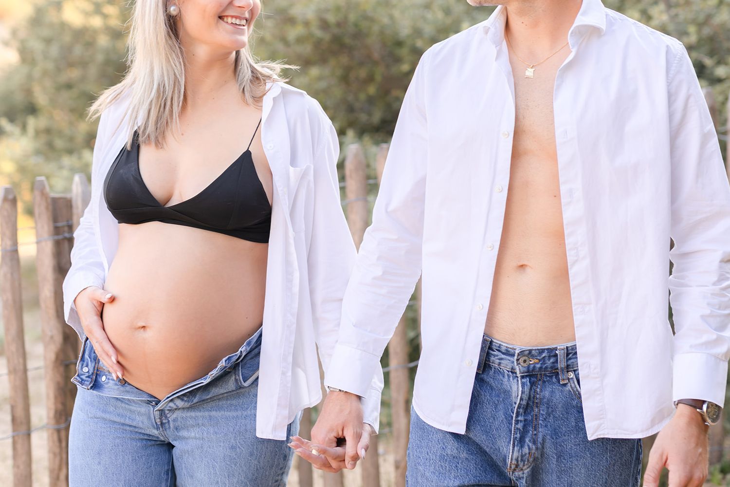 Casual couple in matching white shirts and jeans laughing together during an outdoor photo session.
