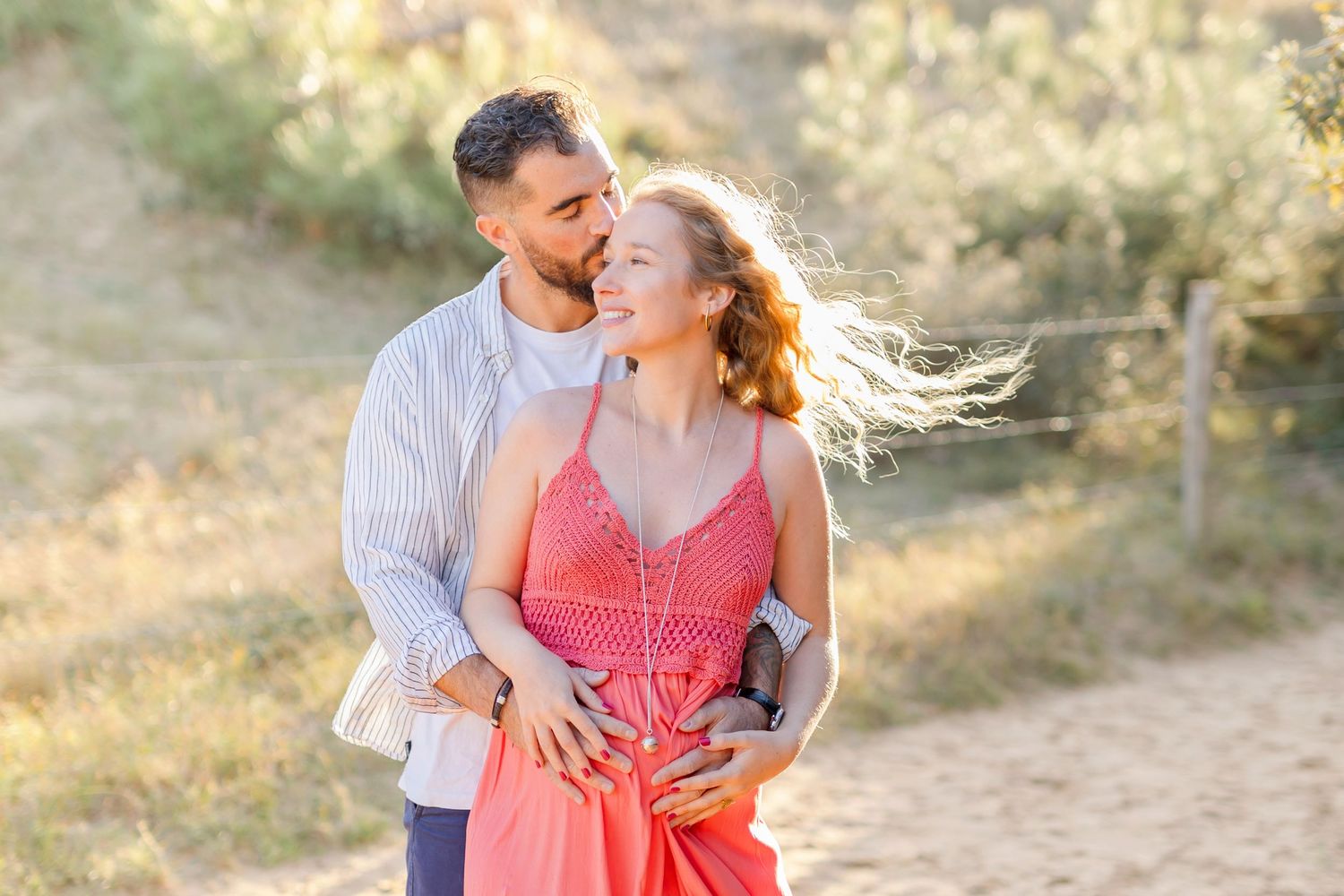 Romantic outdoor maternity photo with couple bathed in golden sunset light.