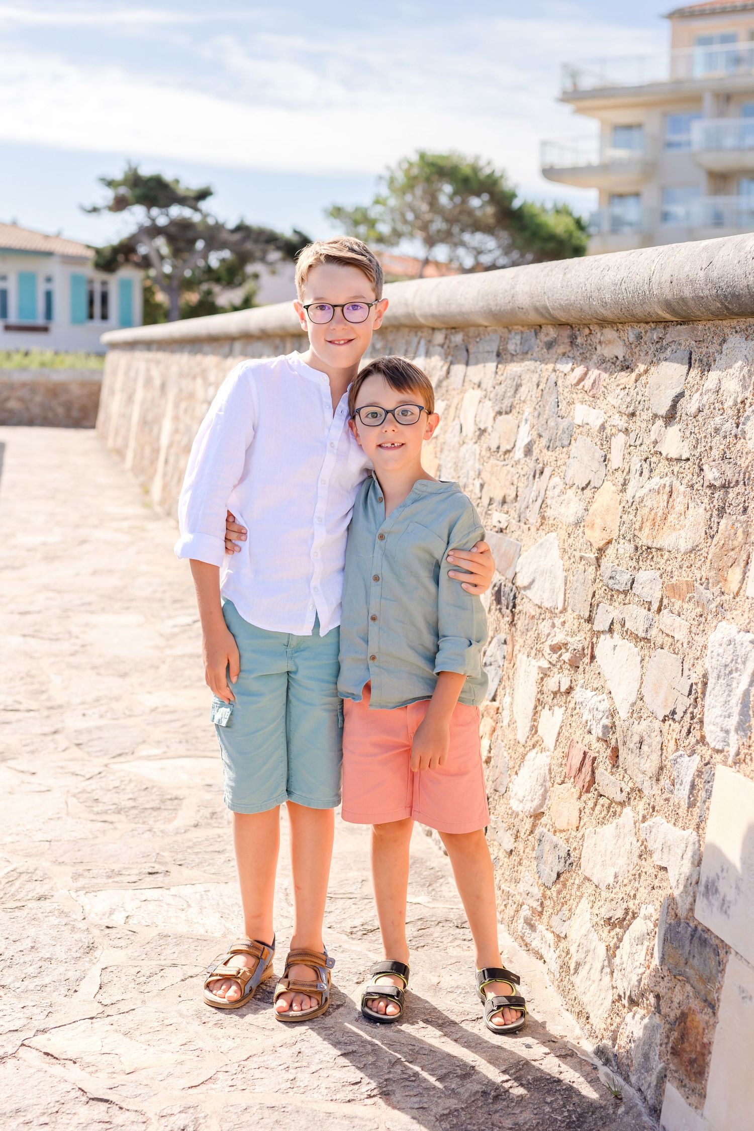 Two young boys in summer clothes standing against stone wall on coastal path.