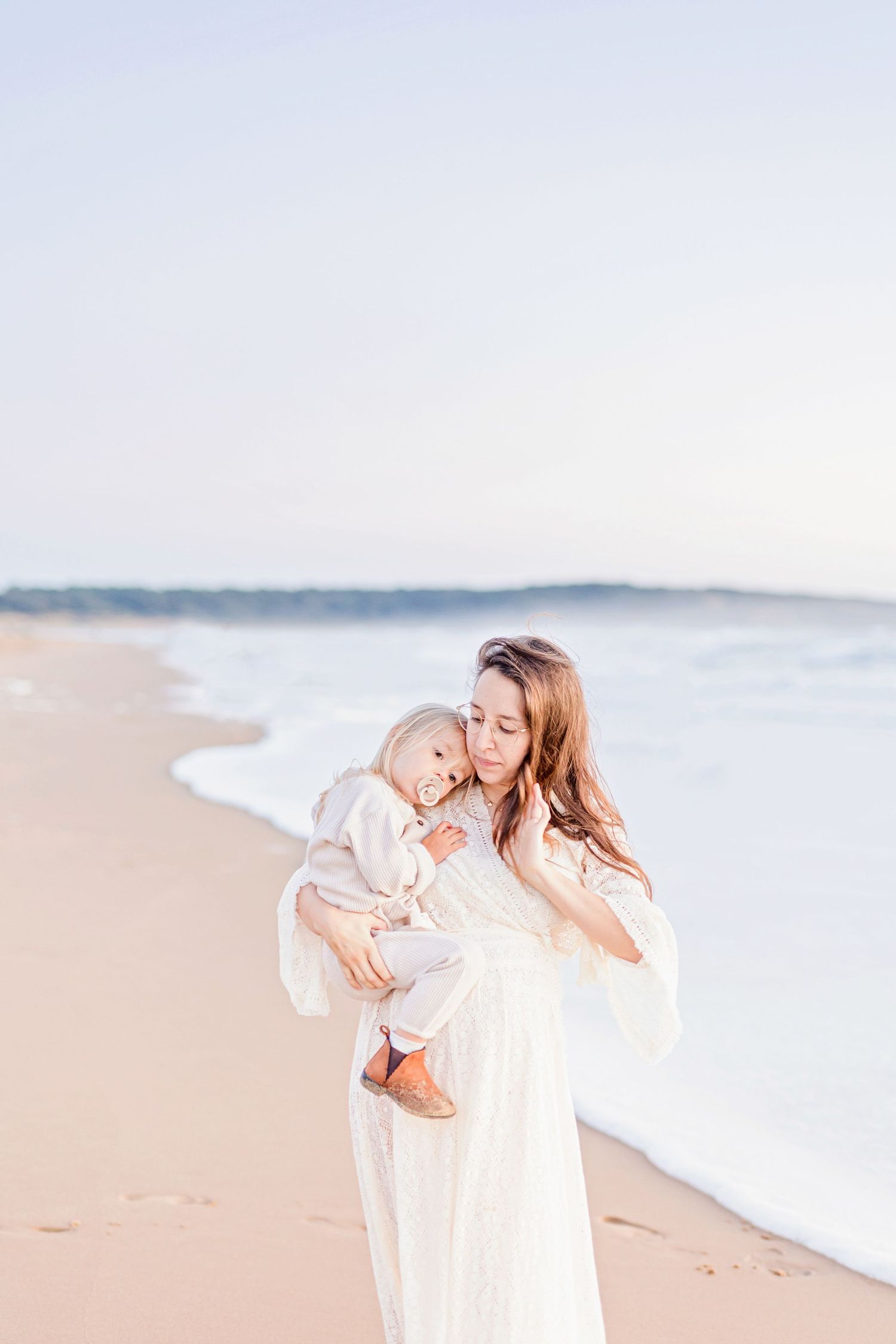 Candid family beach portraits captured in soft pastel tones during golden hour.