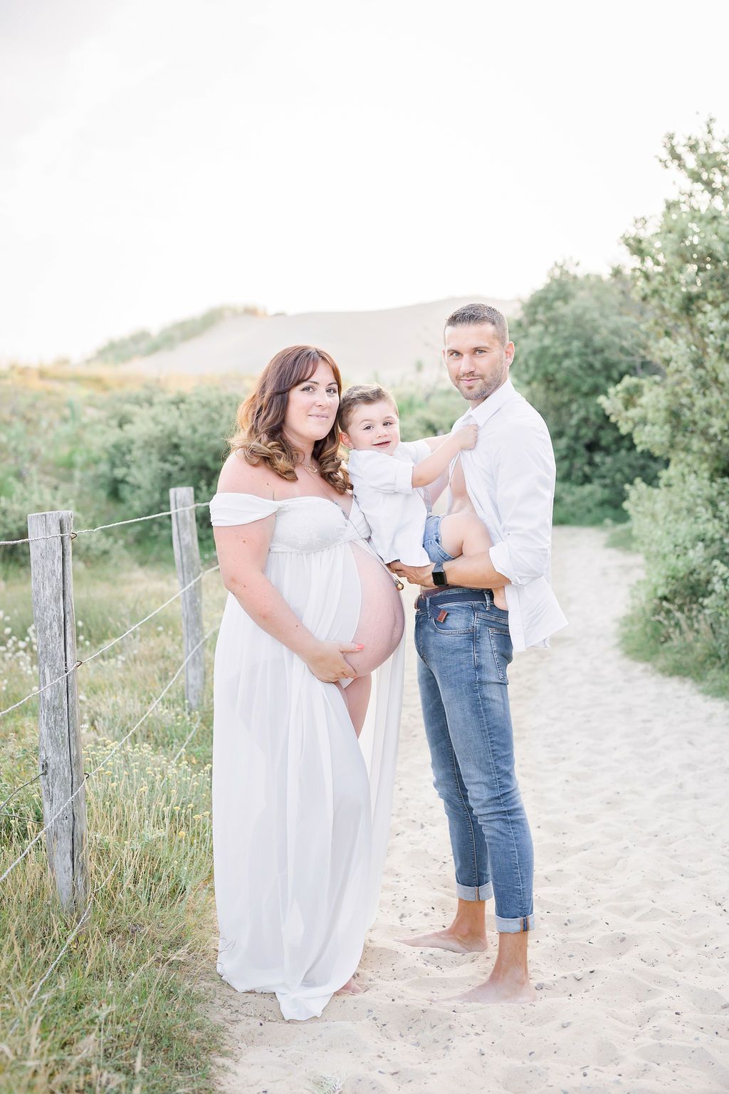 Intimate family photos taken on a sandy coastal path with rustic fencing.