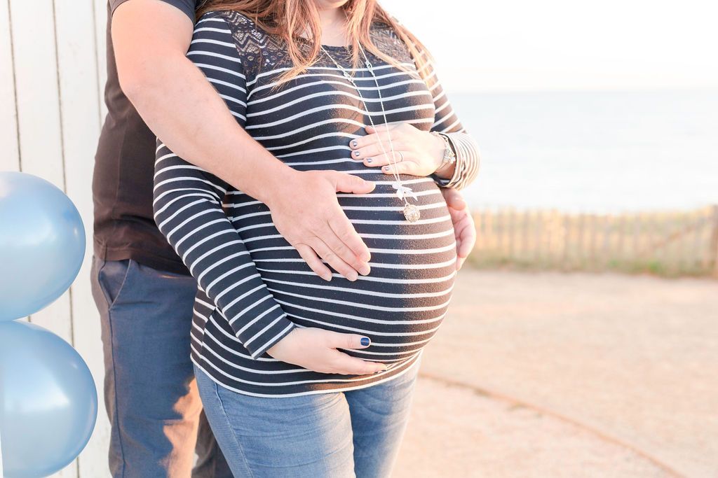 Close-up portrait highlighting pregnant belly with couple's hands in tender embrace.