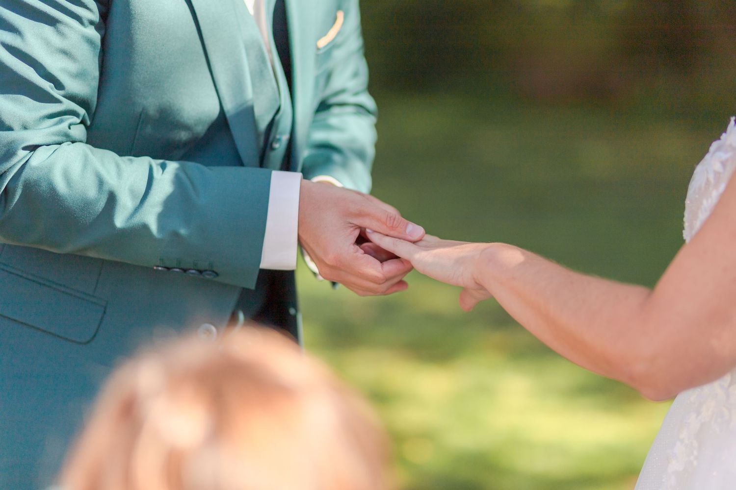 Close-up detail of hands exchanging items during an outdoor ceremony.