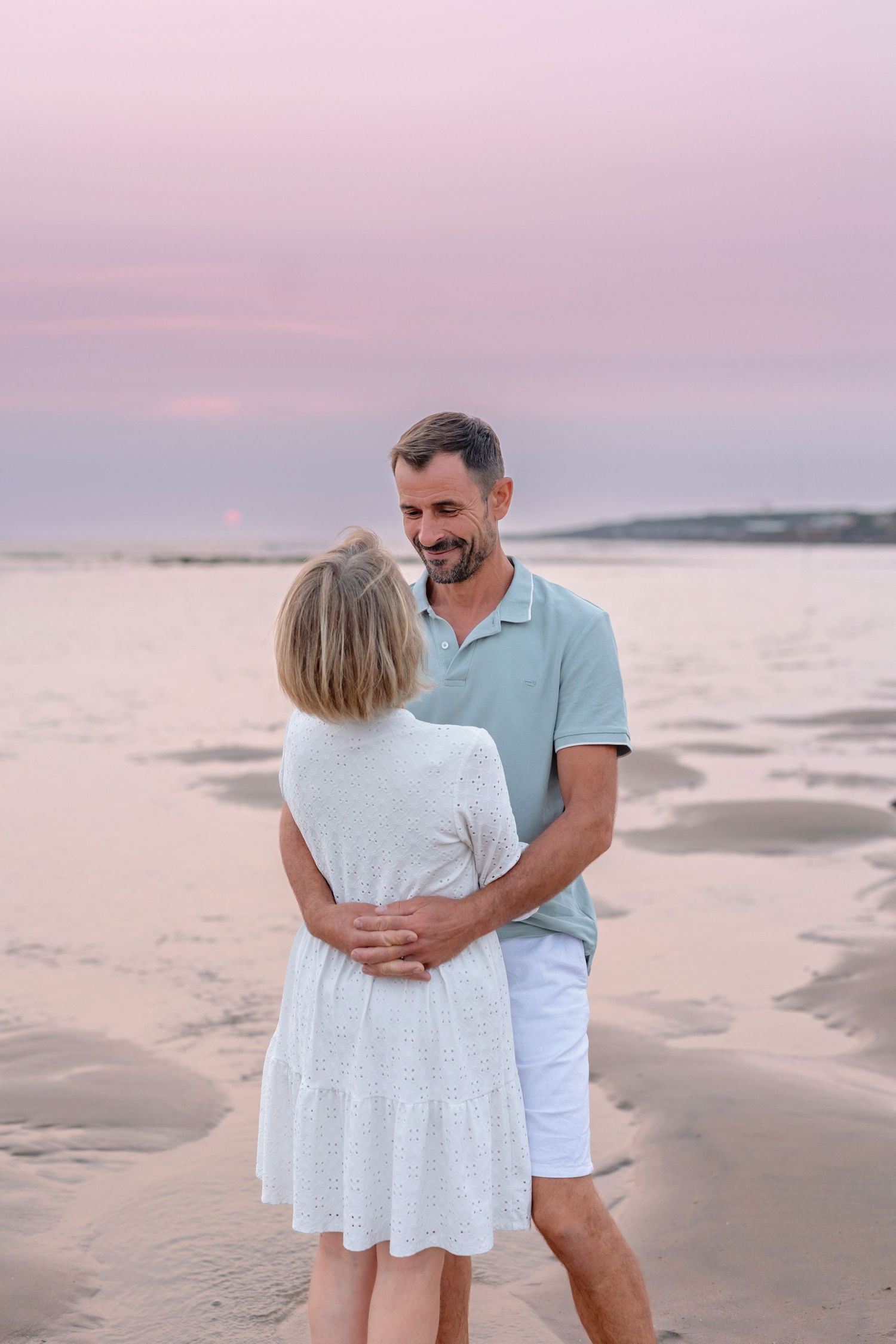 Couple in casual summer attire embracing on beach at sunset.