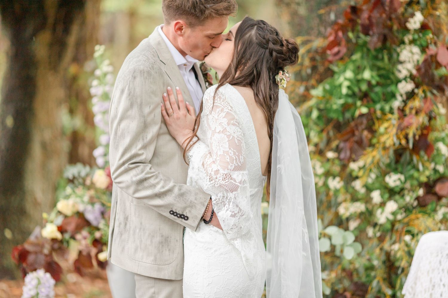 A tender moment between newlyweds surrounded by flowering foliage at an outdoor wedding.