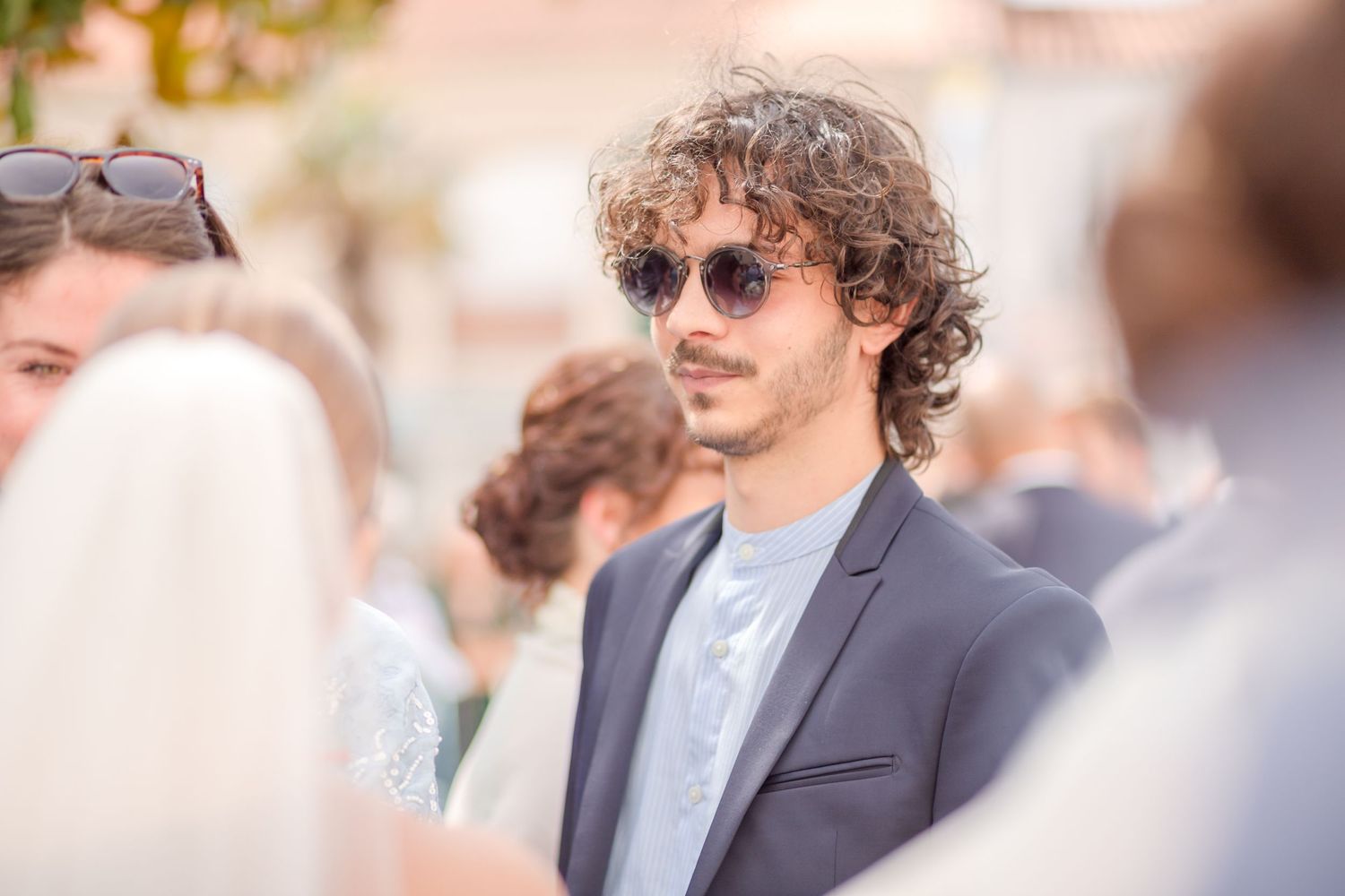 A wedding guest in sunglasses and suit mingles during an outdoor reception.
