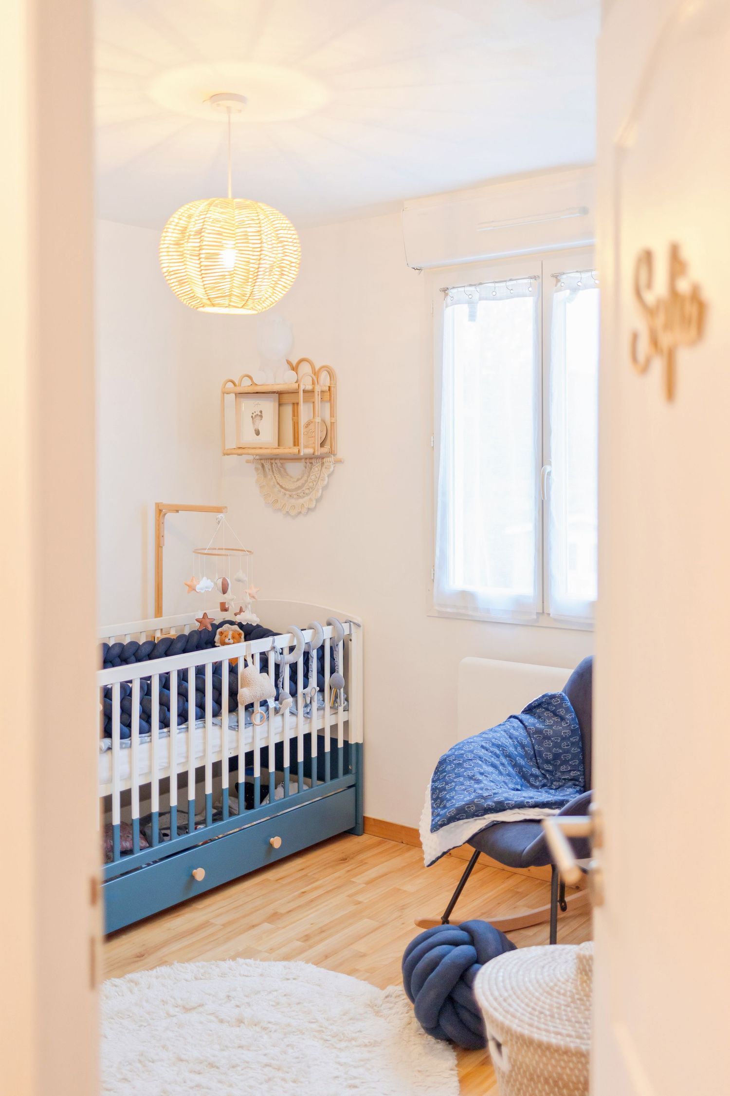 Modern nursery with blue crib, woven pendant light, and natural wood accents.