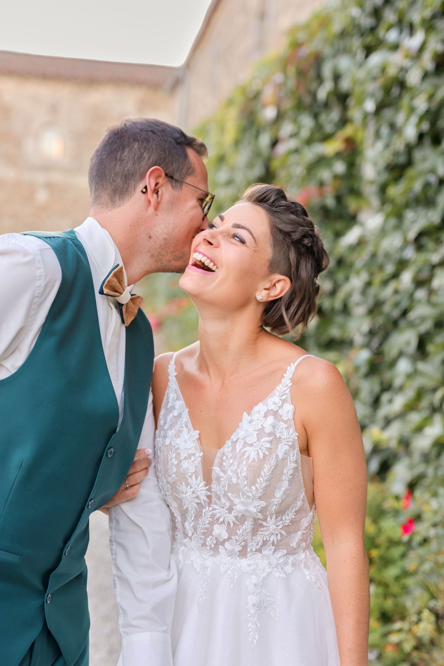 Joyful wedding moment captured against ivy-covered wall background.
