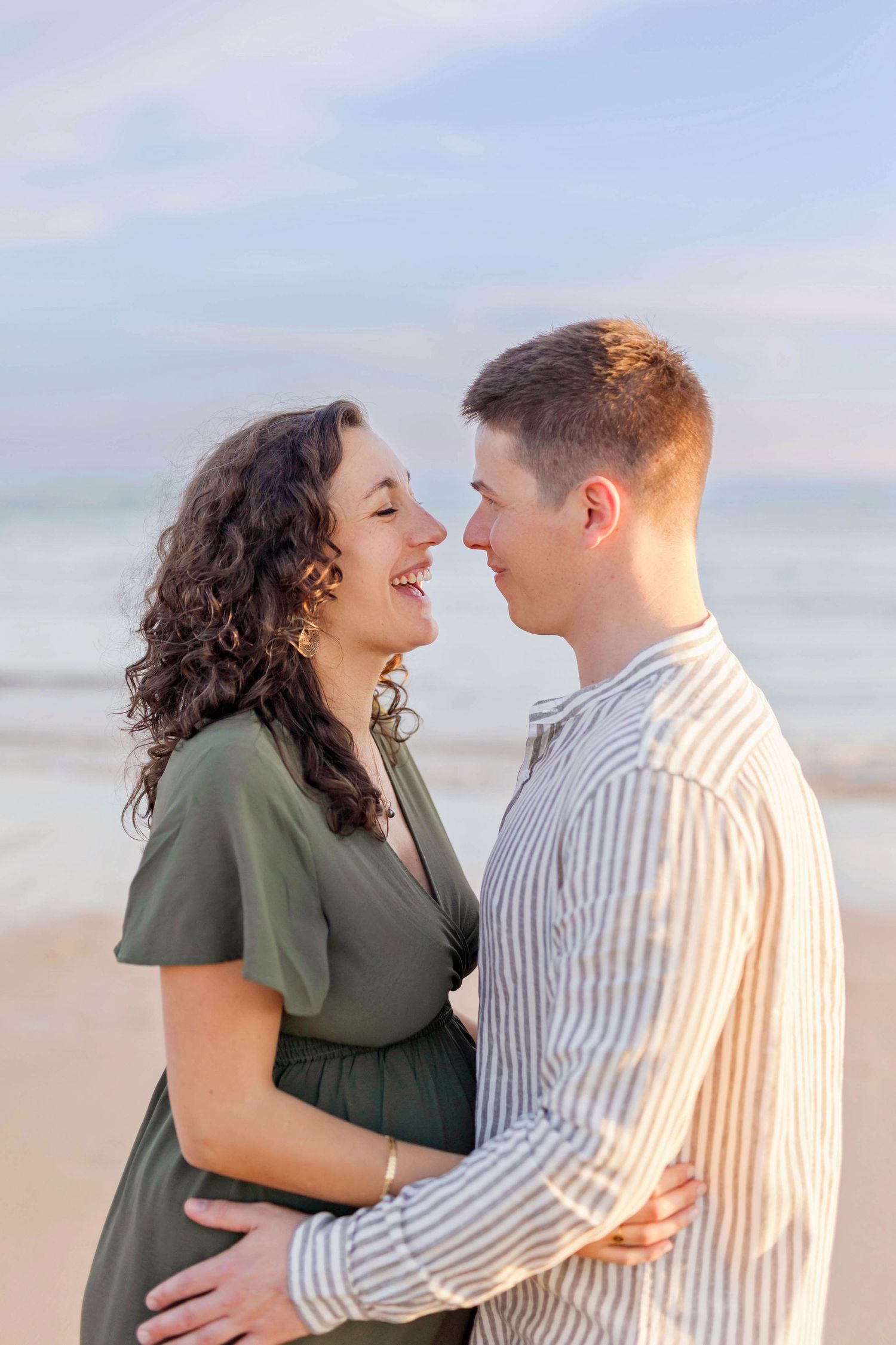 A romantic couple embraces on the beach at sunset wearing coordinated green and white outfits.