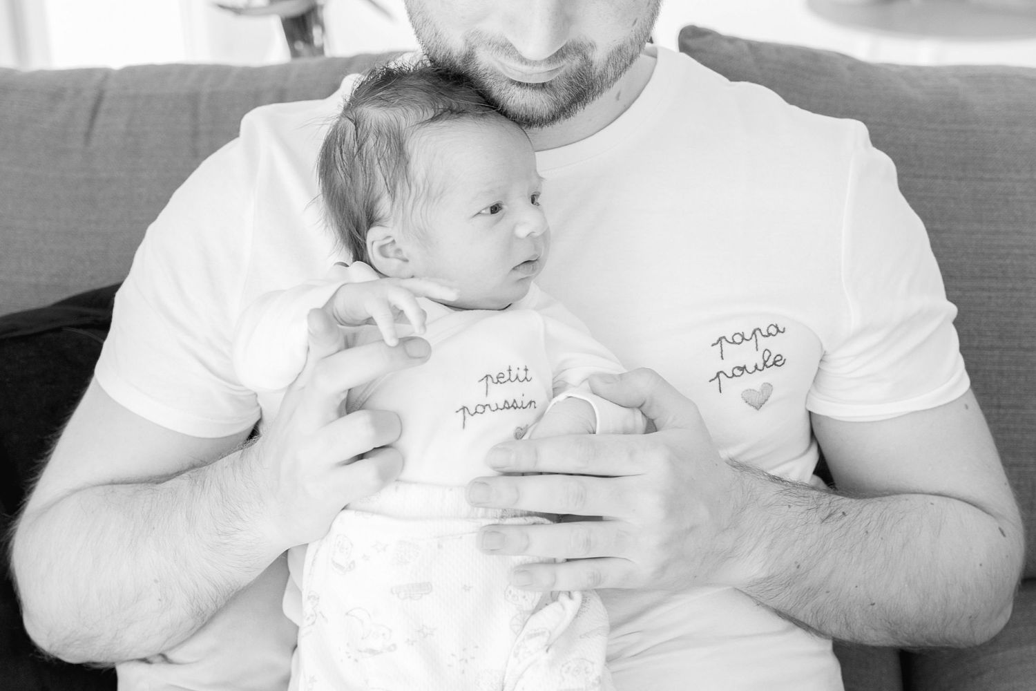 Black and white photo of parent cradling sleeping infant on couch.
