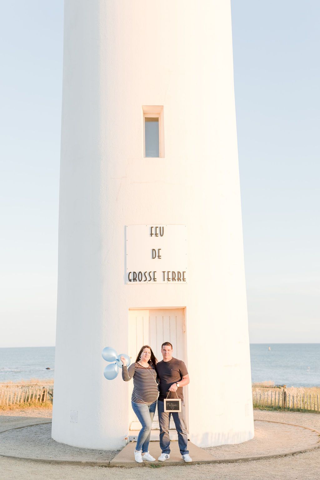 Maternity photo session at Grosse Terre lighthouse with blue balloons and ocean backdrop.