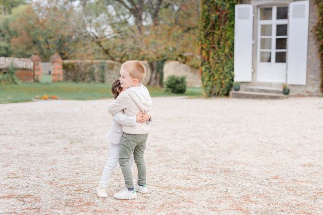 Toddlers play together on gravel path near stone building.