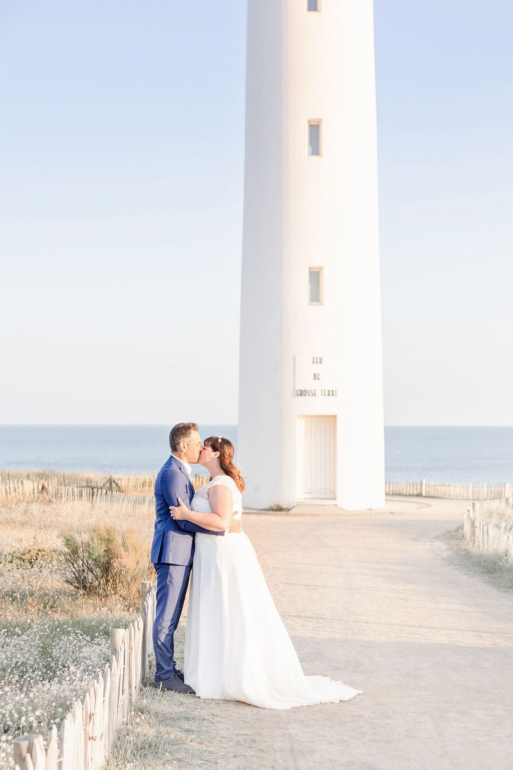 A romantic lighthouse wedding photo with a couple sharing an intimate moment by the sea.