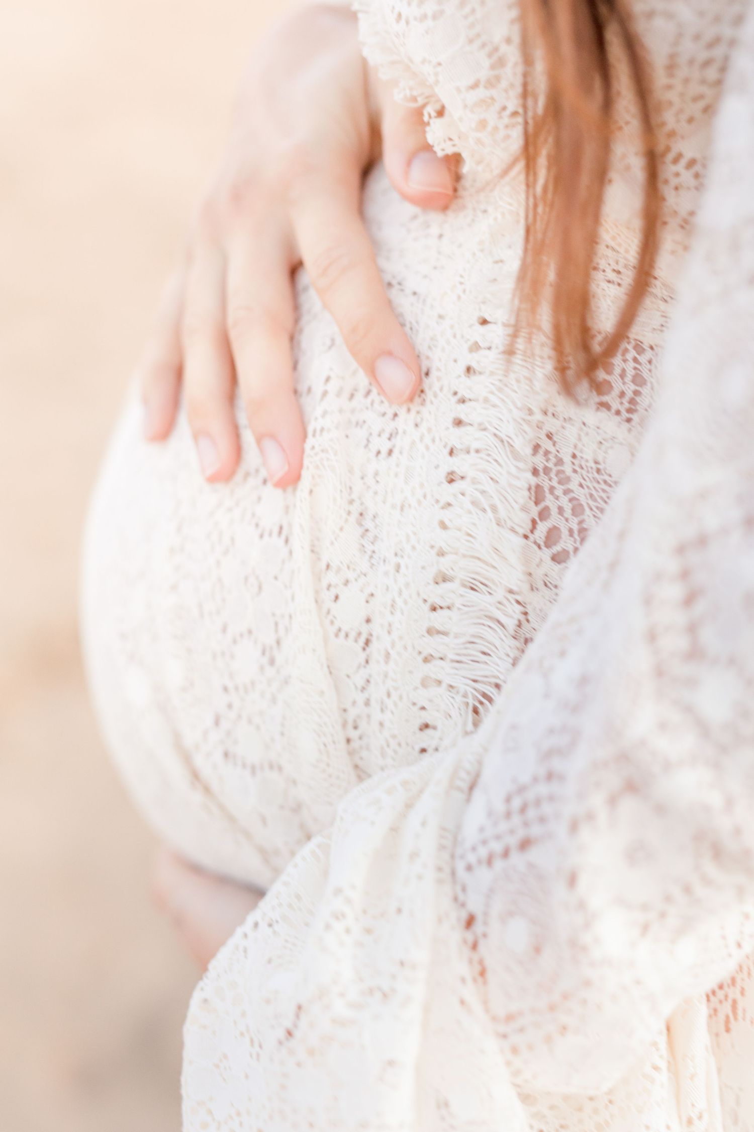 Close-up detail of hands tenderly touching a pregnant belly through white lace fabric.