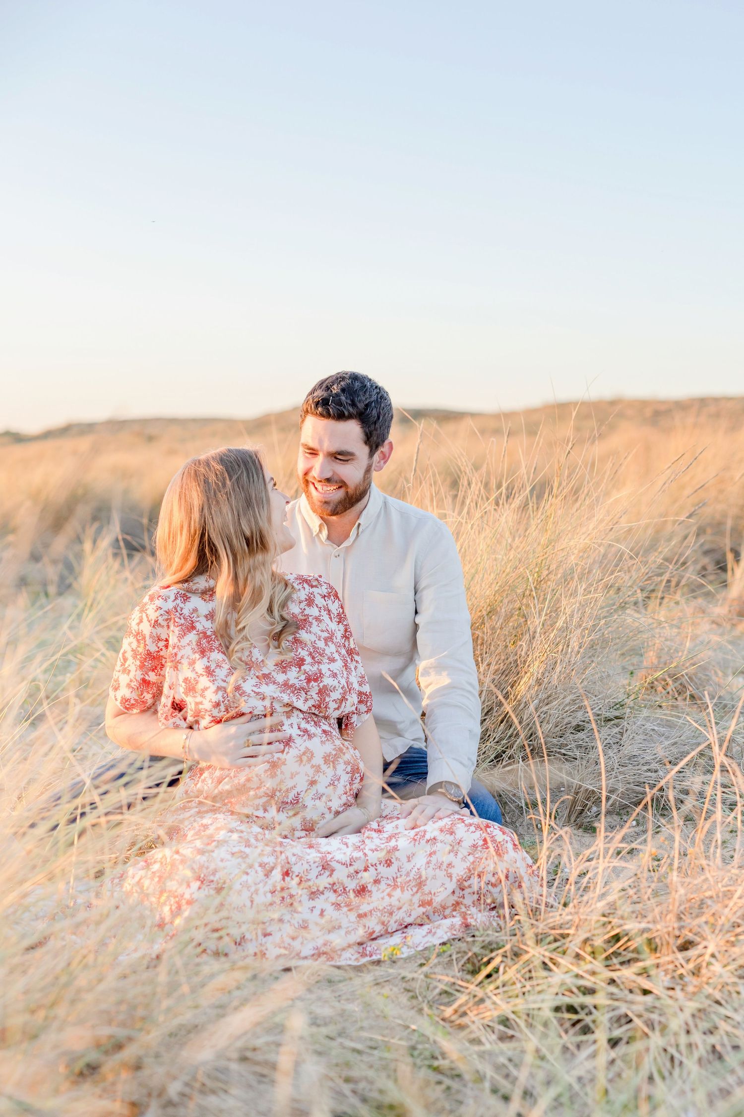 A couple shares an intimate moment while sitting among tall grass at golden hour.