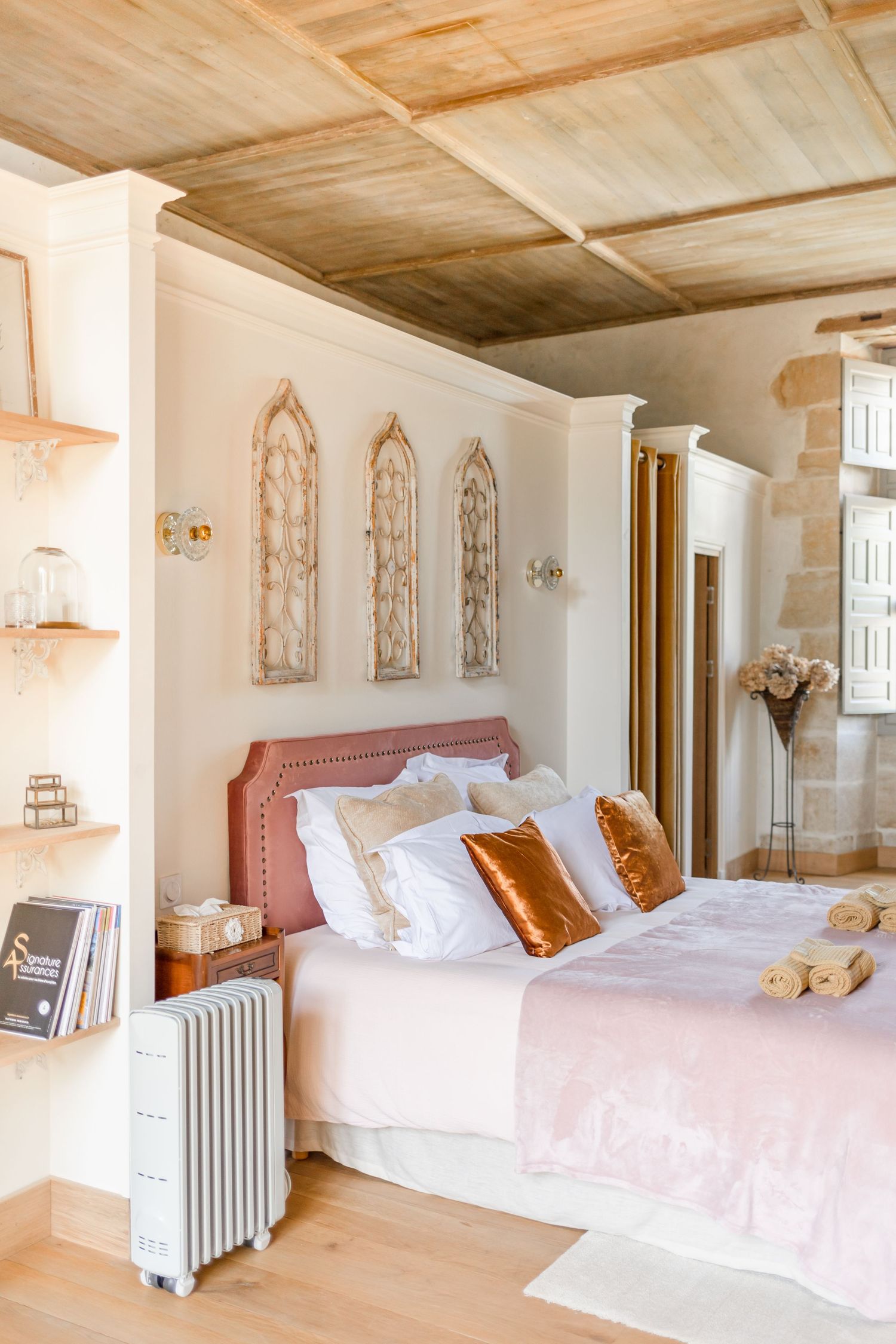Elegant bedroom with wooden ceiling, white bedding, and gothic-style wall decor.