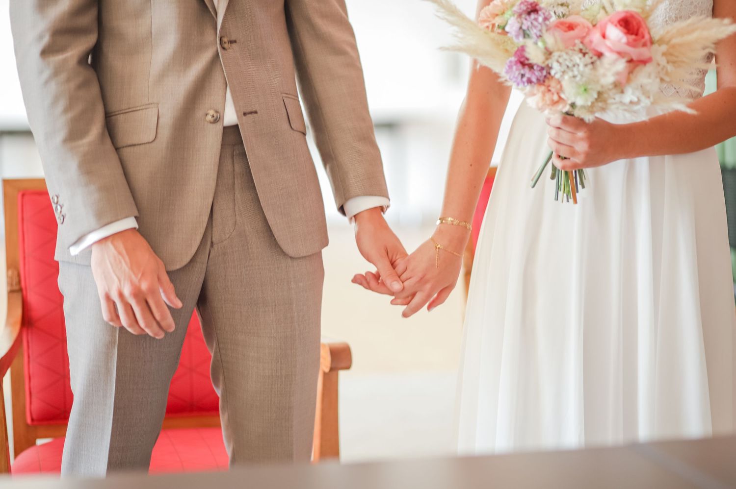 Detail shot of formal wedding attire showing tan suit jackets and white dress fabric.