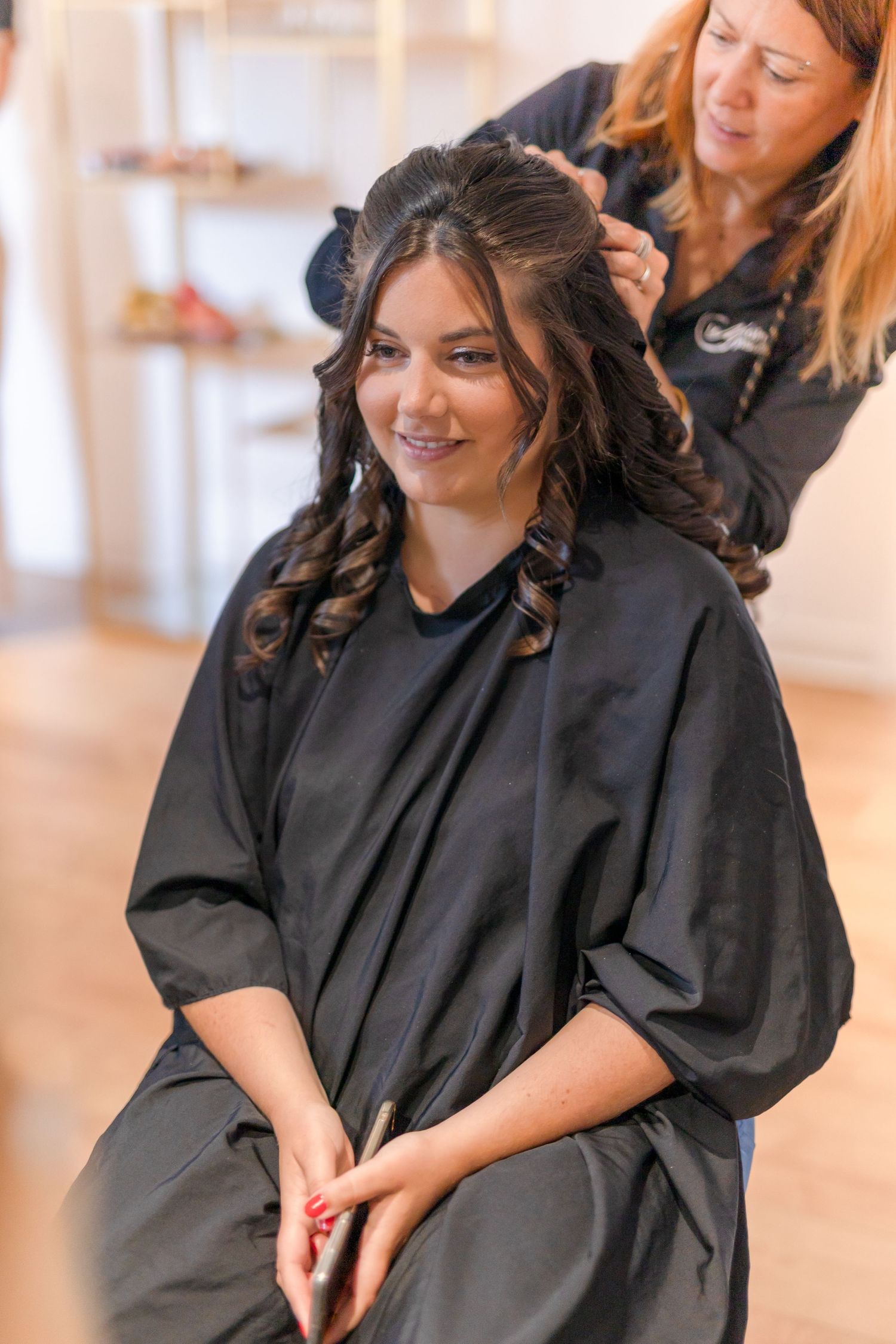 A hairstylist works on styling dark curly hair during a beauty preparation session.