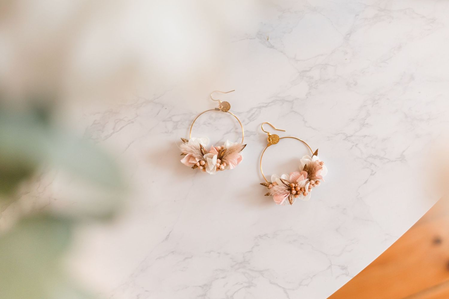 Dainty gold floral earrings with peach dried flowers on marble surface.