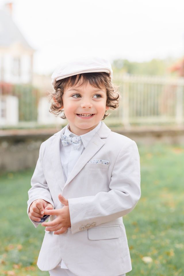 Child in formal white outfit smiles and plays in an outdoor setting.