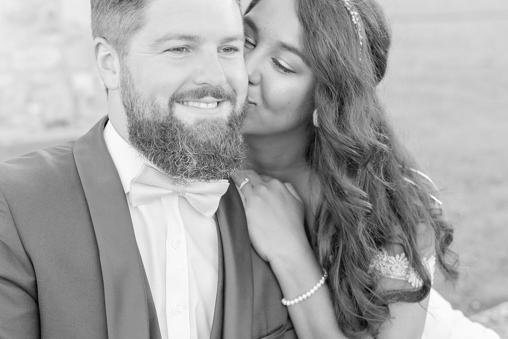 Black and white portrait of newlyweds sharing an intimate moment with the bride kissing her groom's cheek.