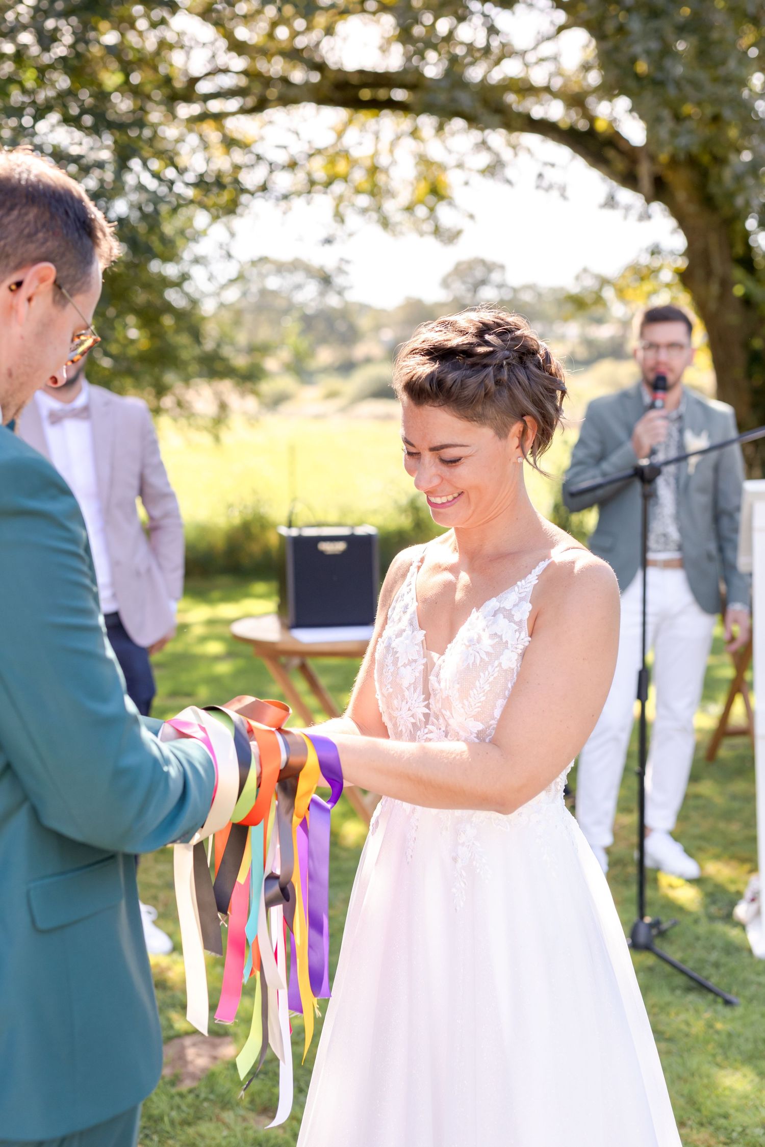 Outdoor wedding moment capturing white lace dress and teal suit details with vibrant ribbons.