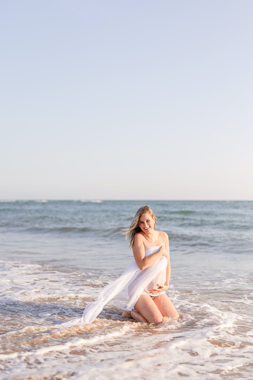 A serene beach photography sequence showing a person in flowy white fabric sitting in gentle ocean waves.