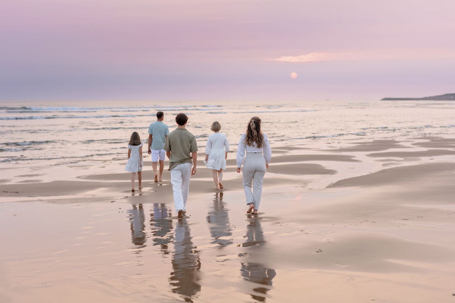 Group walking along reflective wet beach shore at sunset.