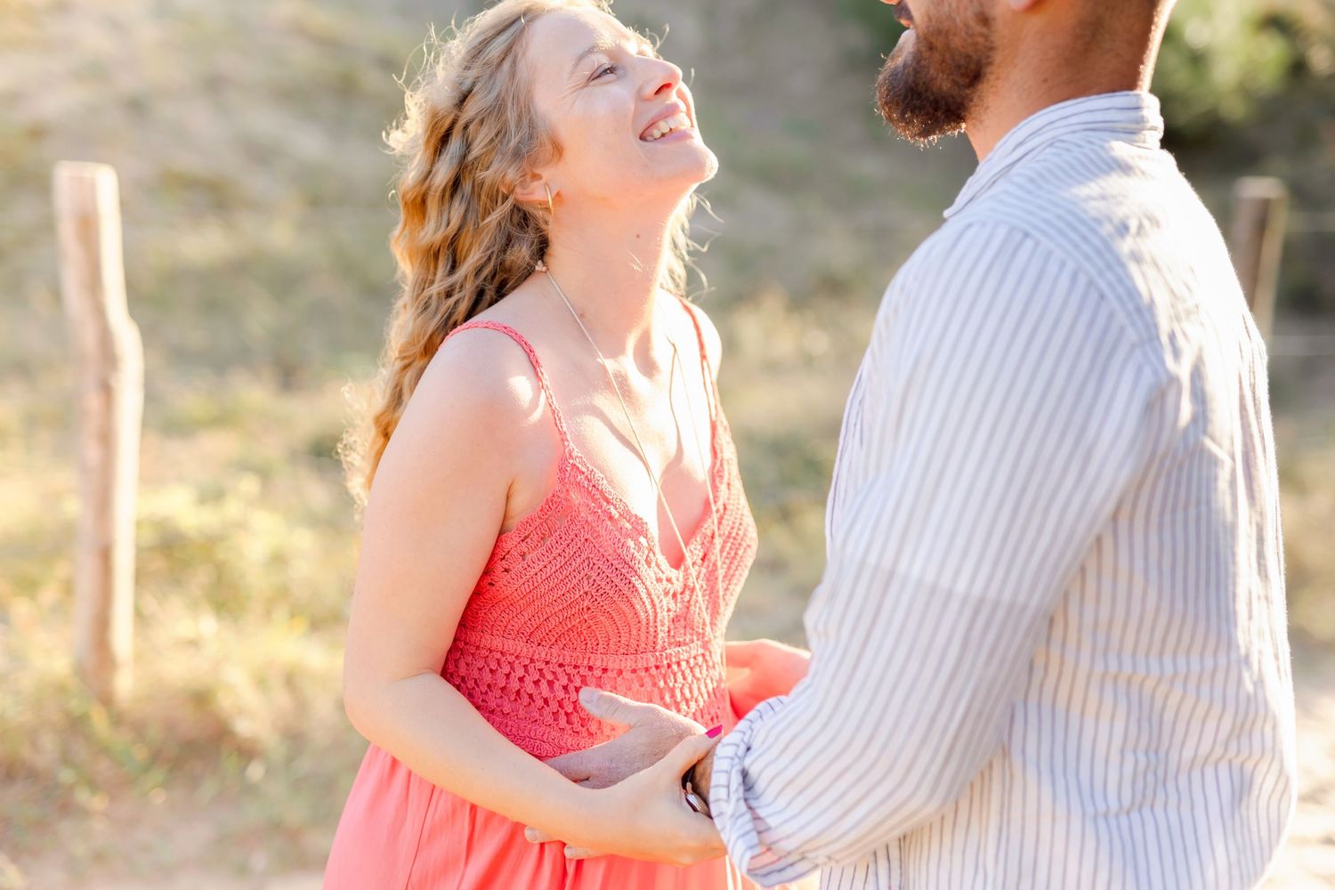 Joyful moment between couple during outdoor maternity shoot with warm sunset lighting.