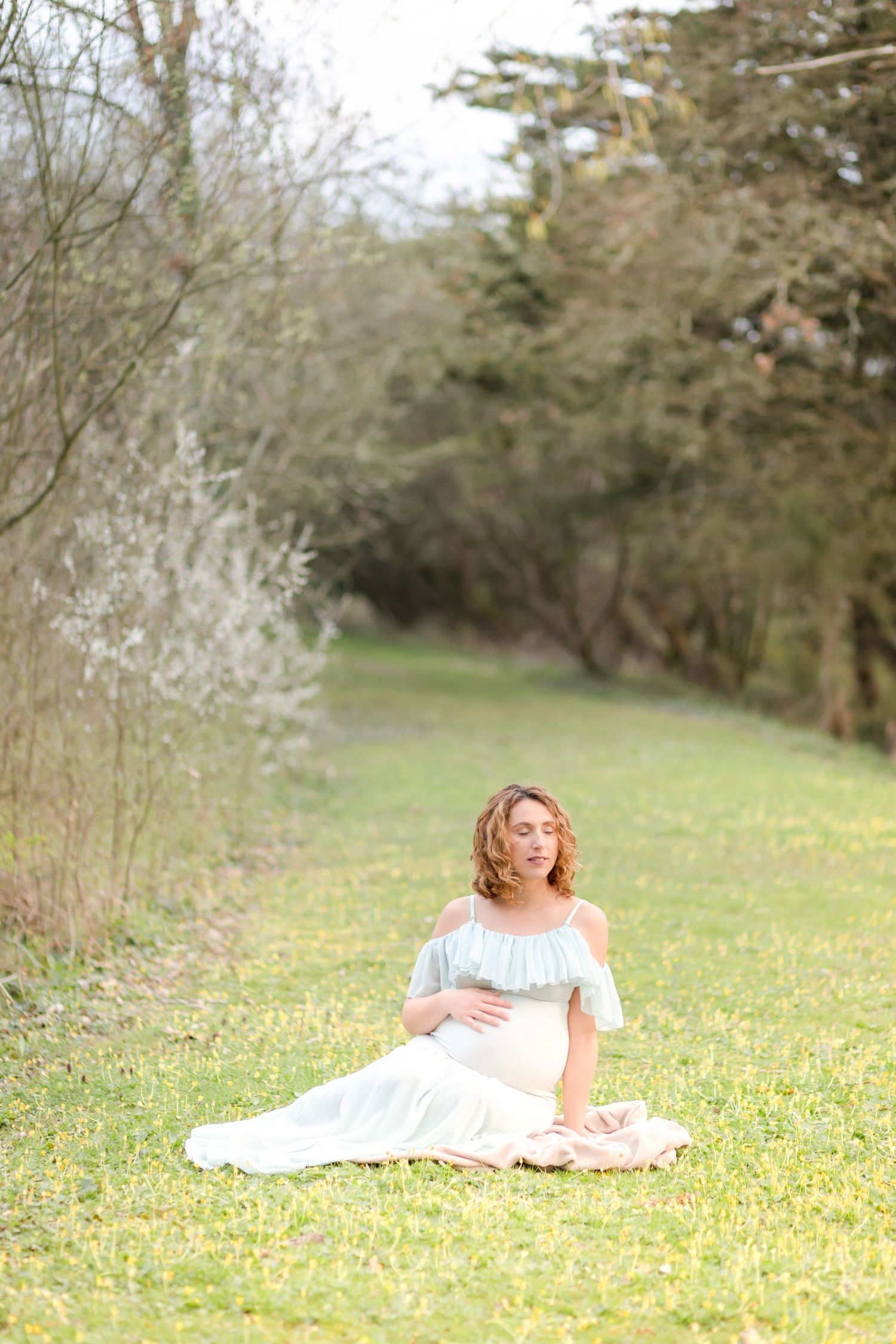 A peaceful maternity photo session in a grassy meadow surrounded by trees.