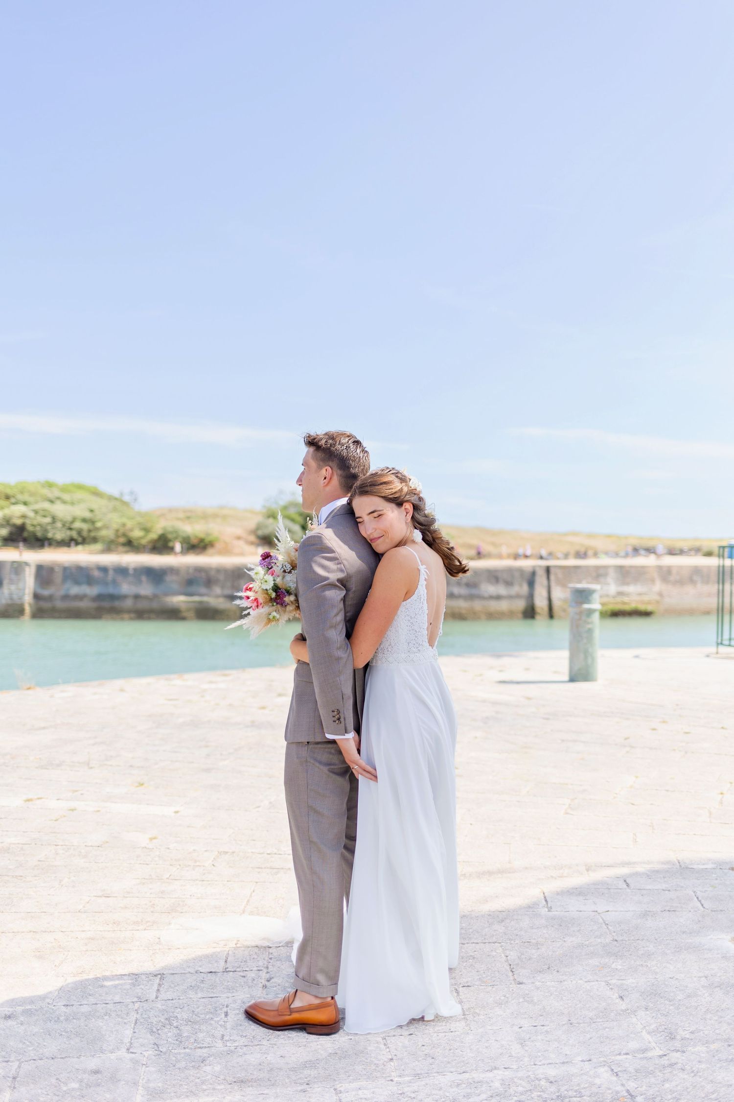 Wedding couple in romantic pose near harbor with lighthouse in background.