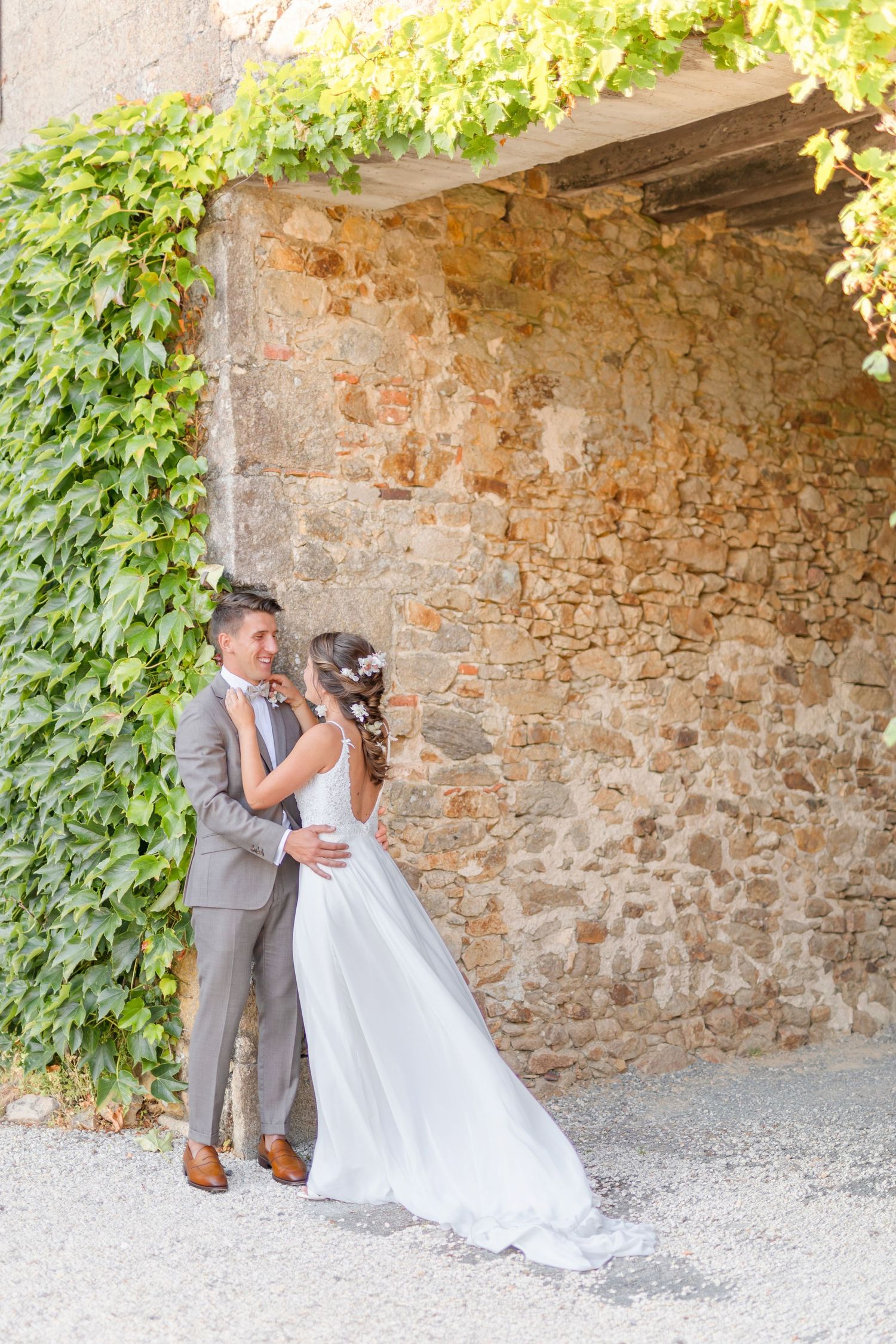 Wedding couple embracing under stone archway with cascading ivy.