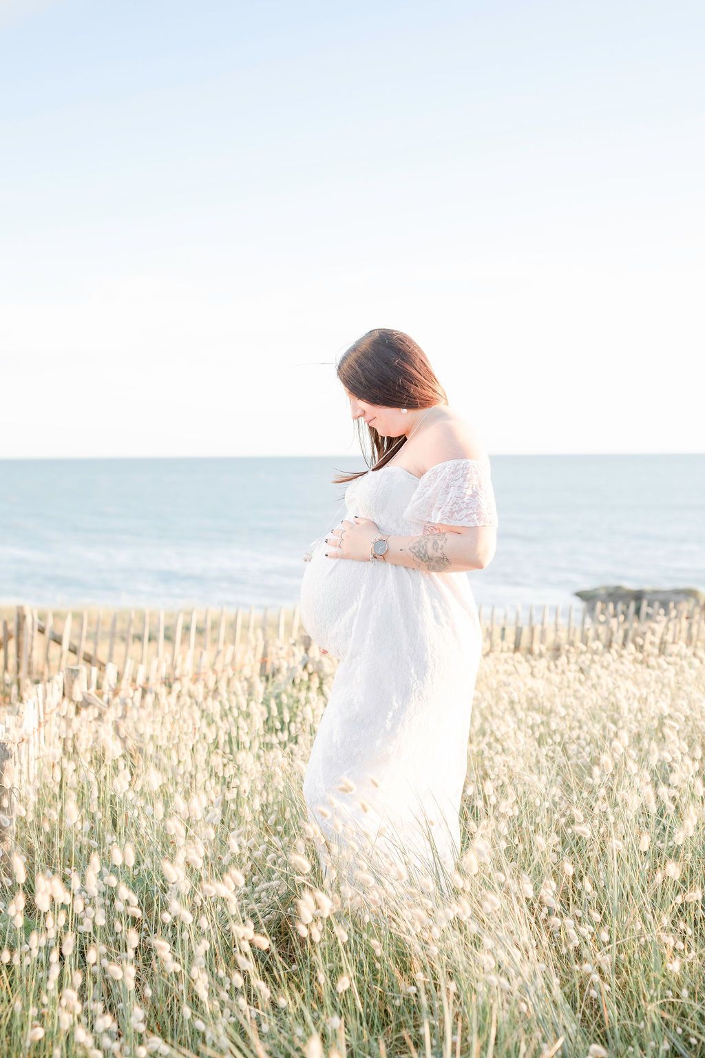Ethereal maternity portrait of woman in white dress among seaside wildflowers.