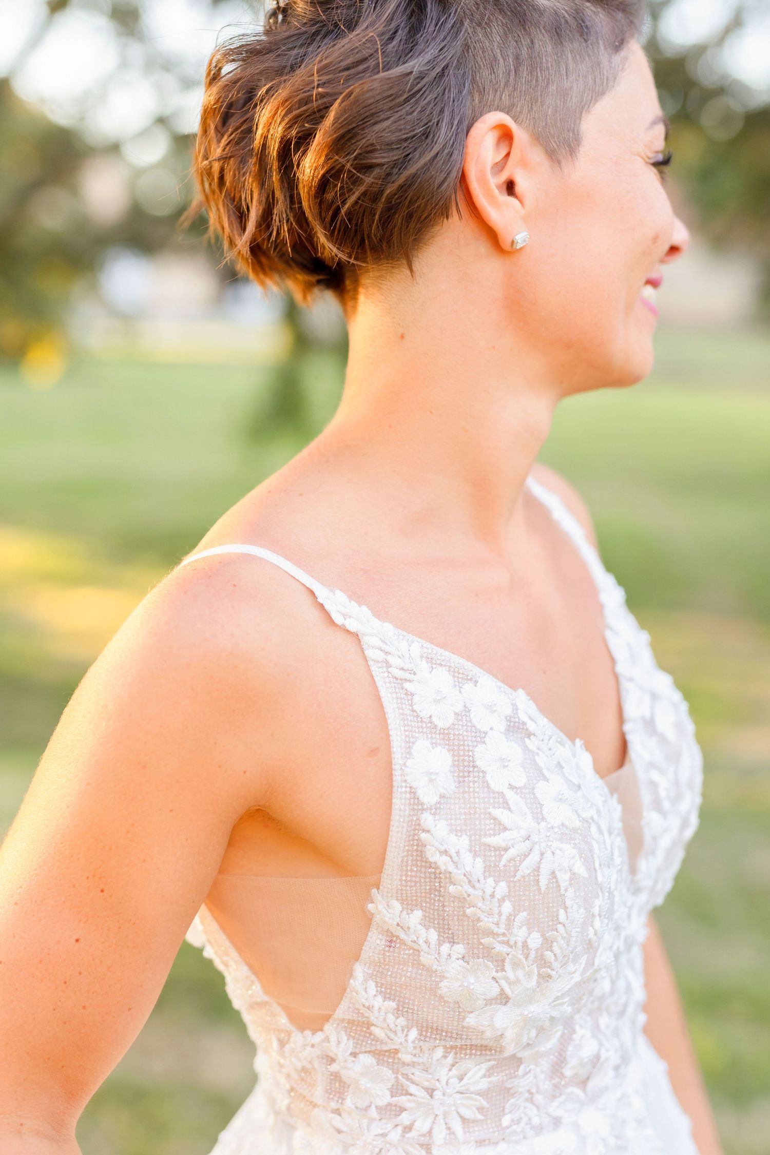 Close-up detail of bride's lace wedding dress and short hairstyle in warm evening light.