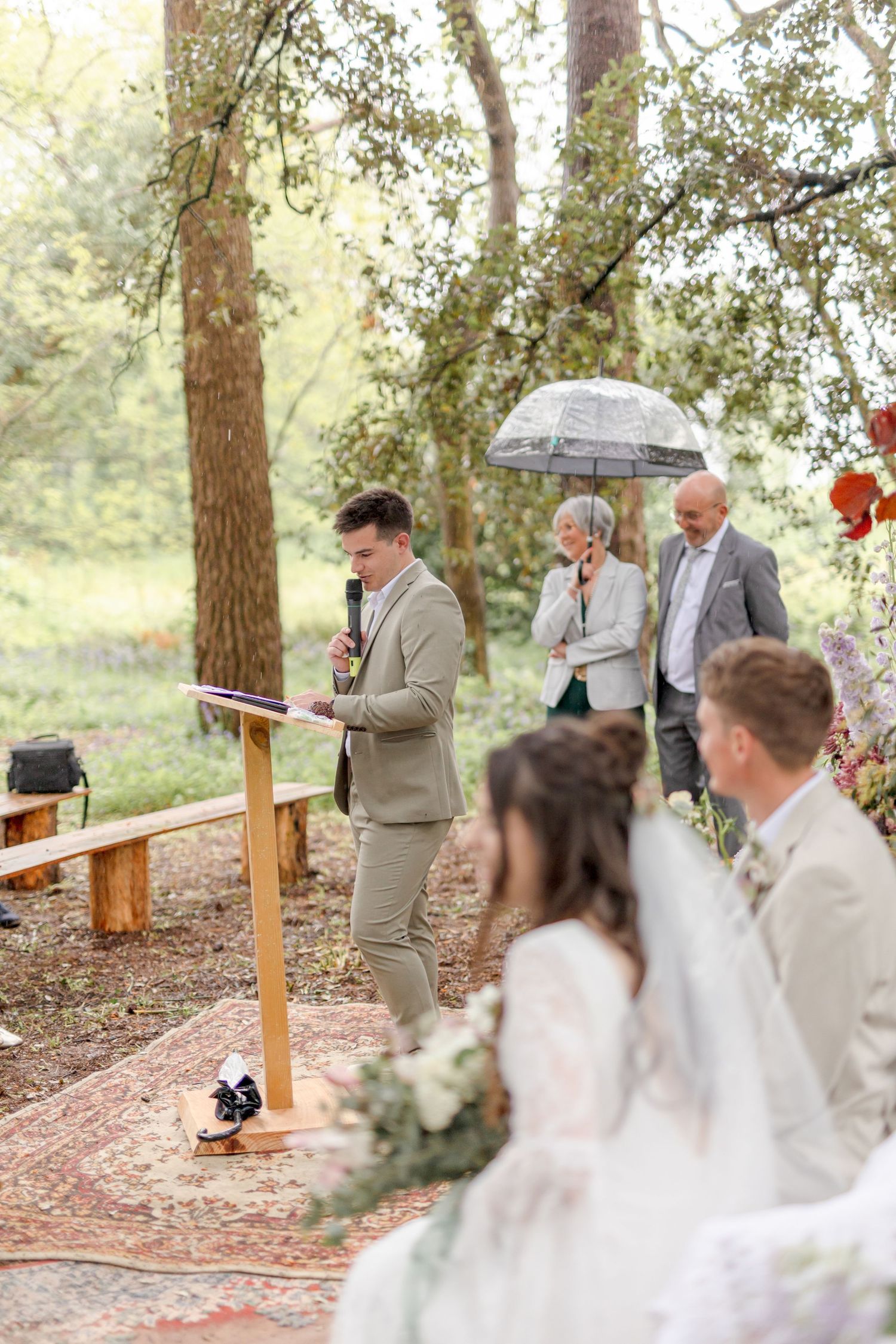 Wedding ceremony in progress along tree-lined forest path with seated guests.