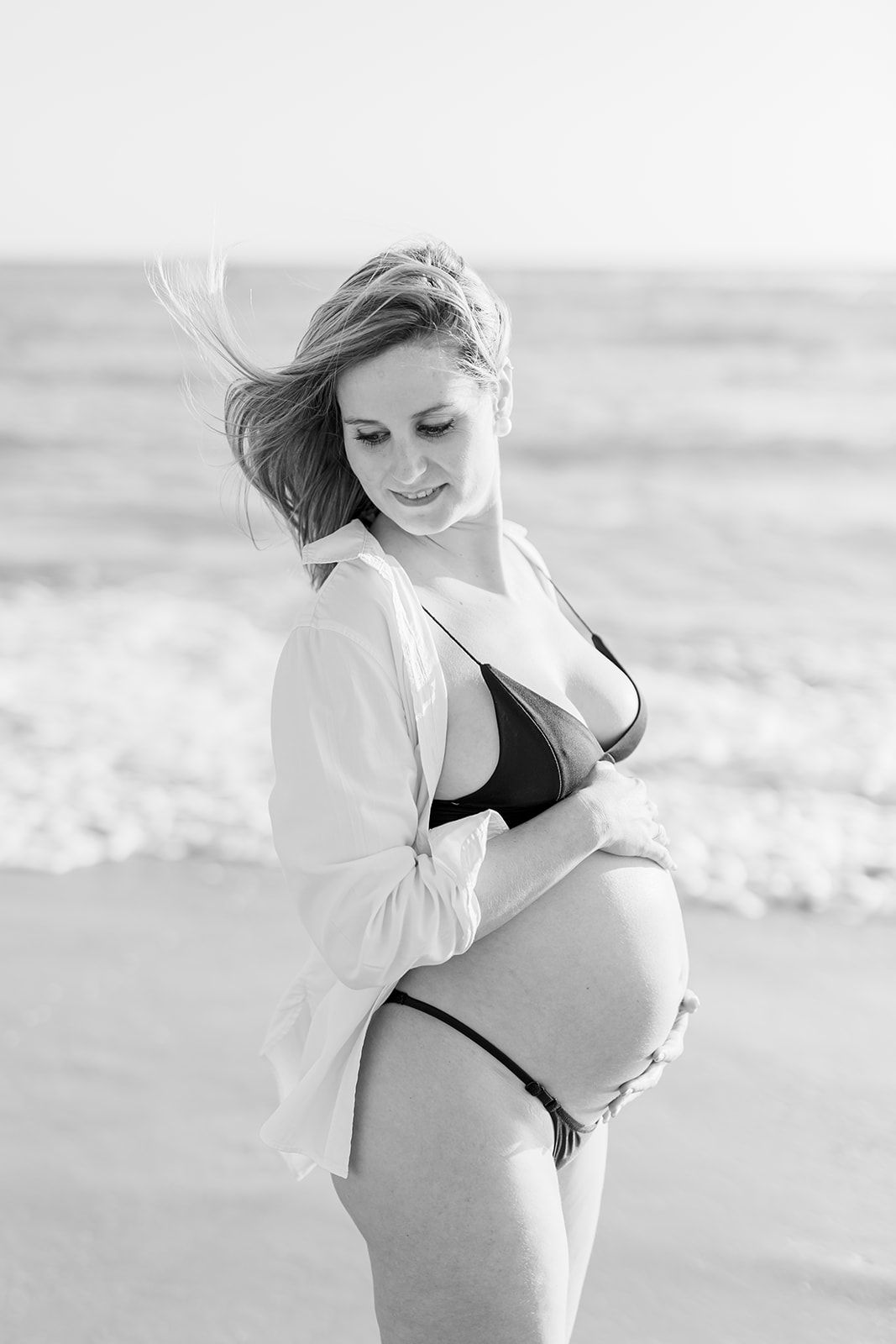 Black and white portrait series of a woman in a bikini and white shirt at the beach in soft natural light.