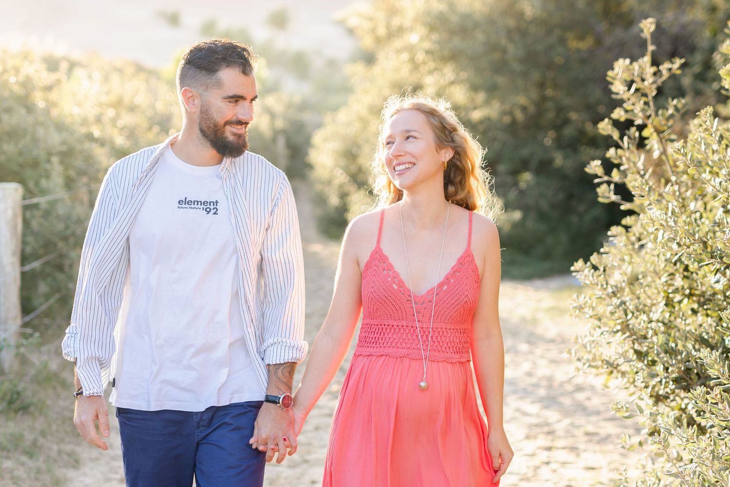 A couple shares a joyful moment while walking on a sandy nature path.