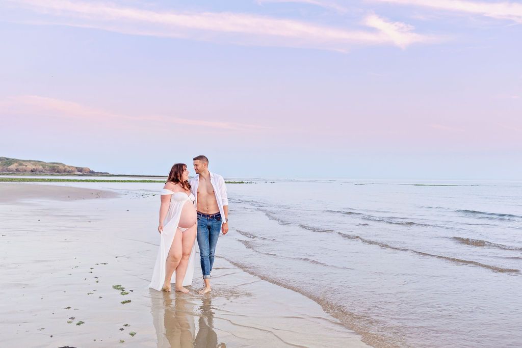 Couple strolling hand in hand on a serene beach during sunset with pink and purple sky.